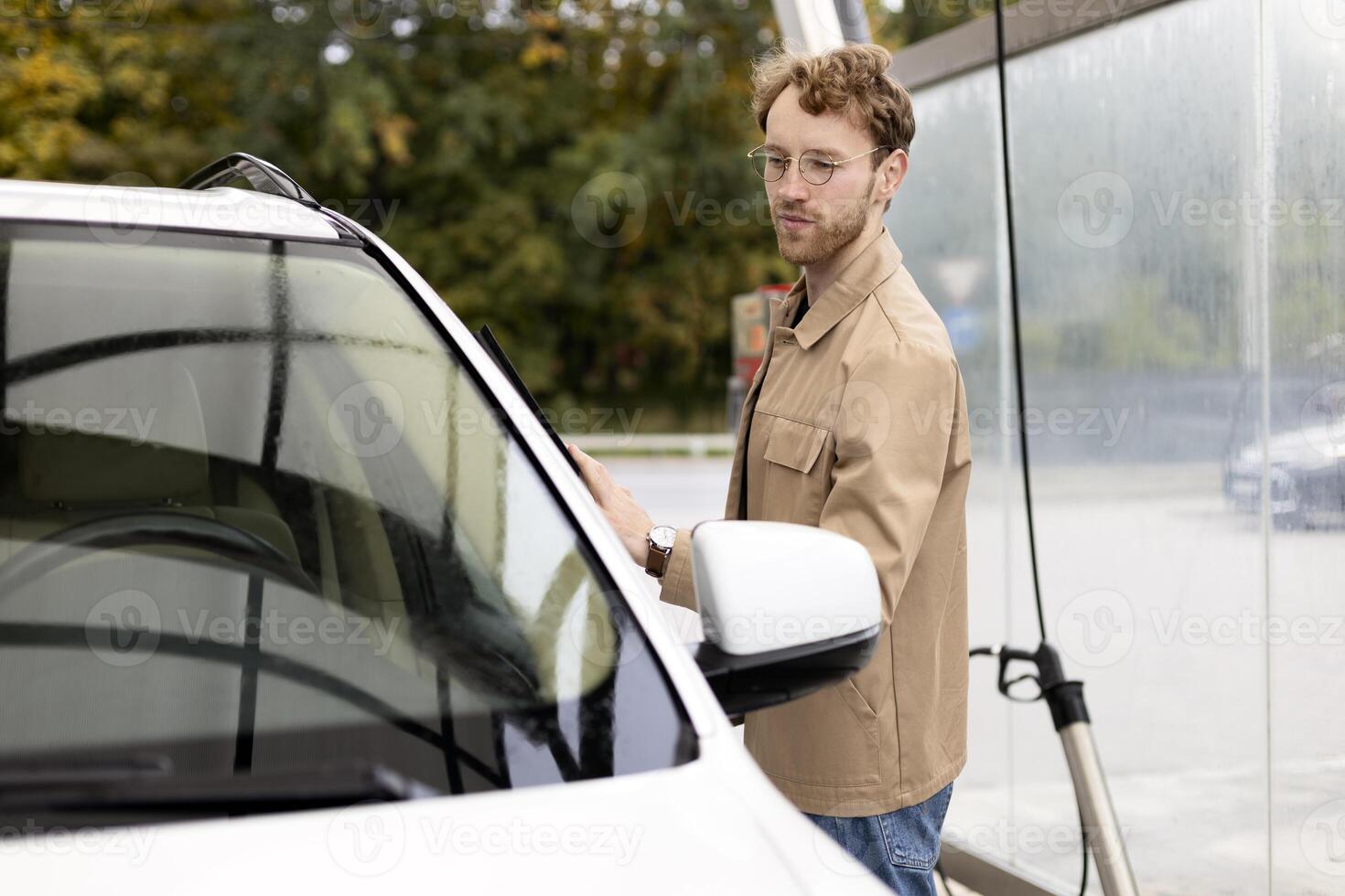 Young driver cleaning car windshield on self service car wash photo