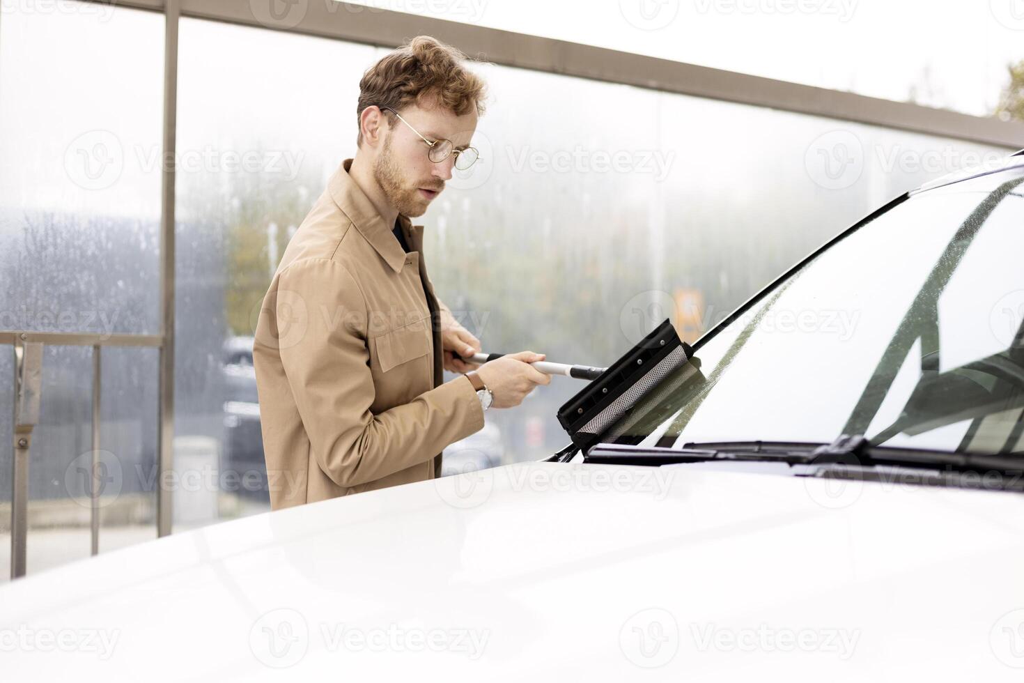 Young man is cleaning car windshield with scraper and snow brush photo
