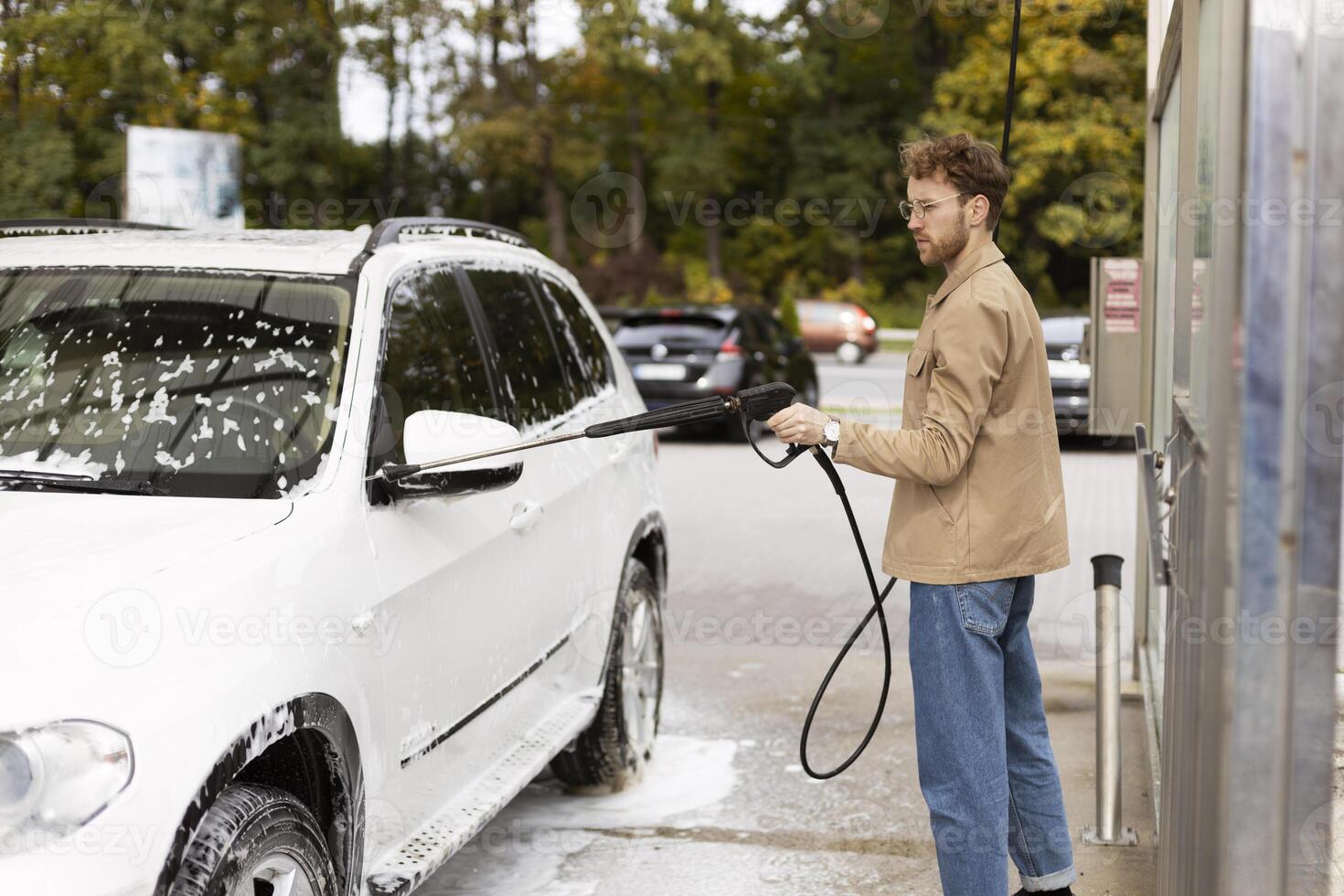 Man washing his car with a pressure washer at a self service car wash photo
