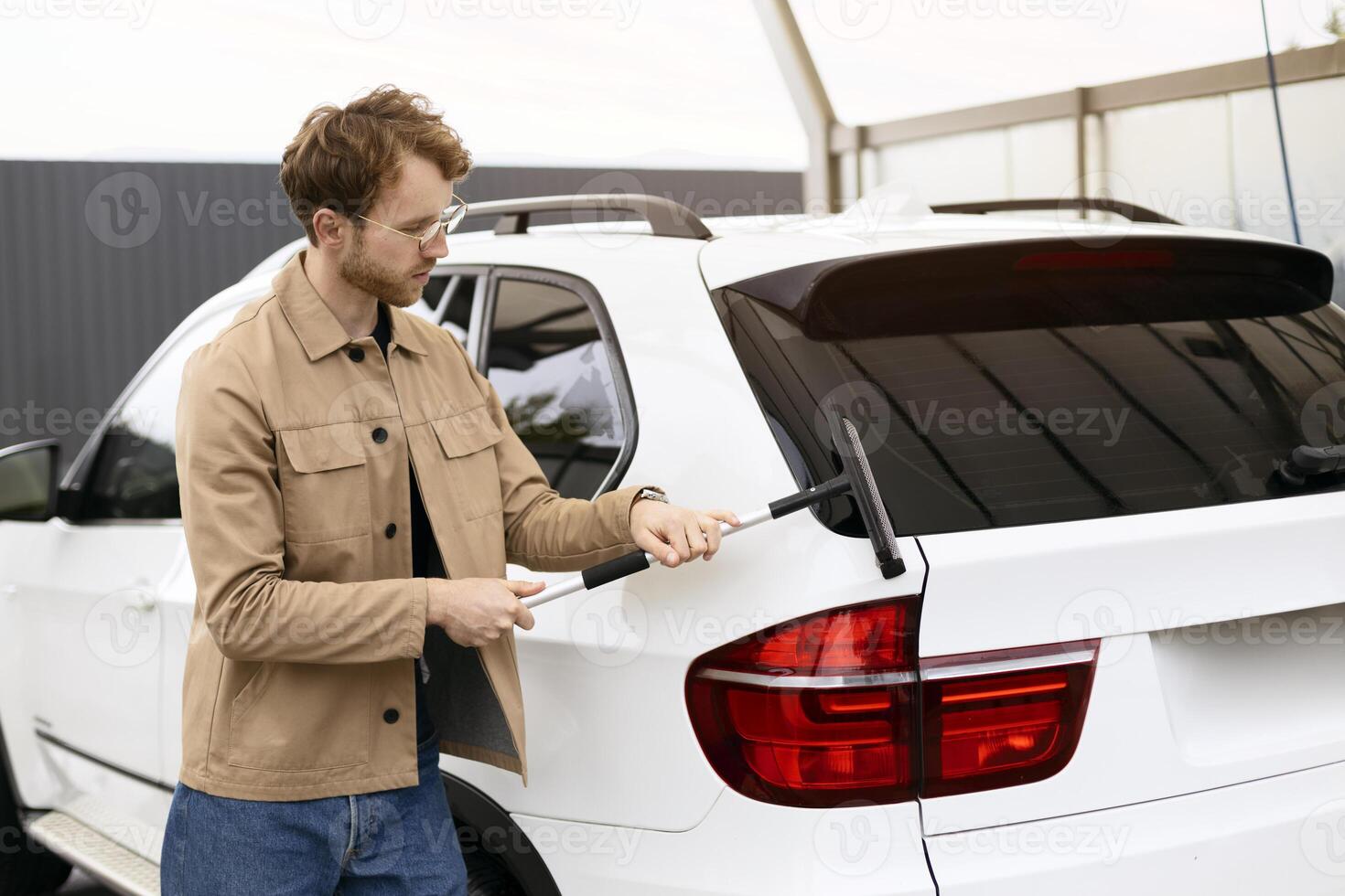 Young man cleaning car rear window with squeegee photo