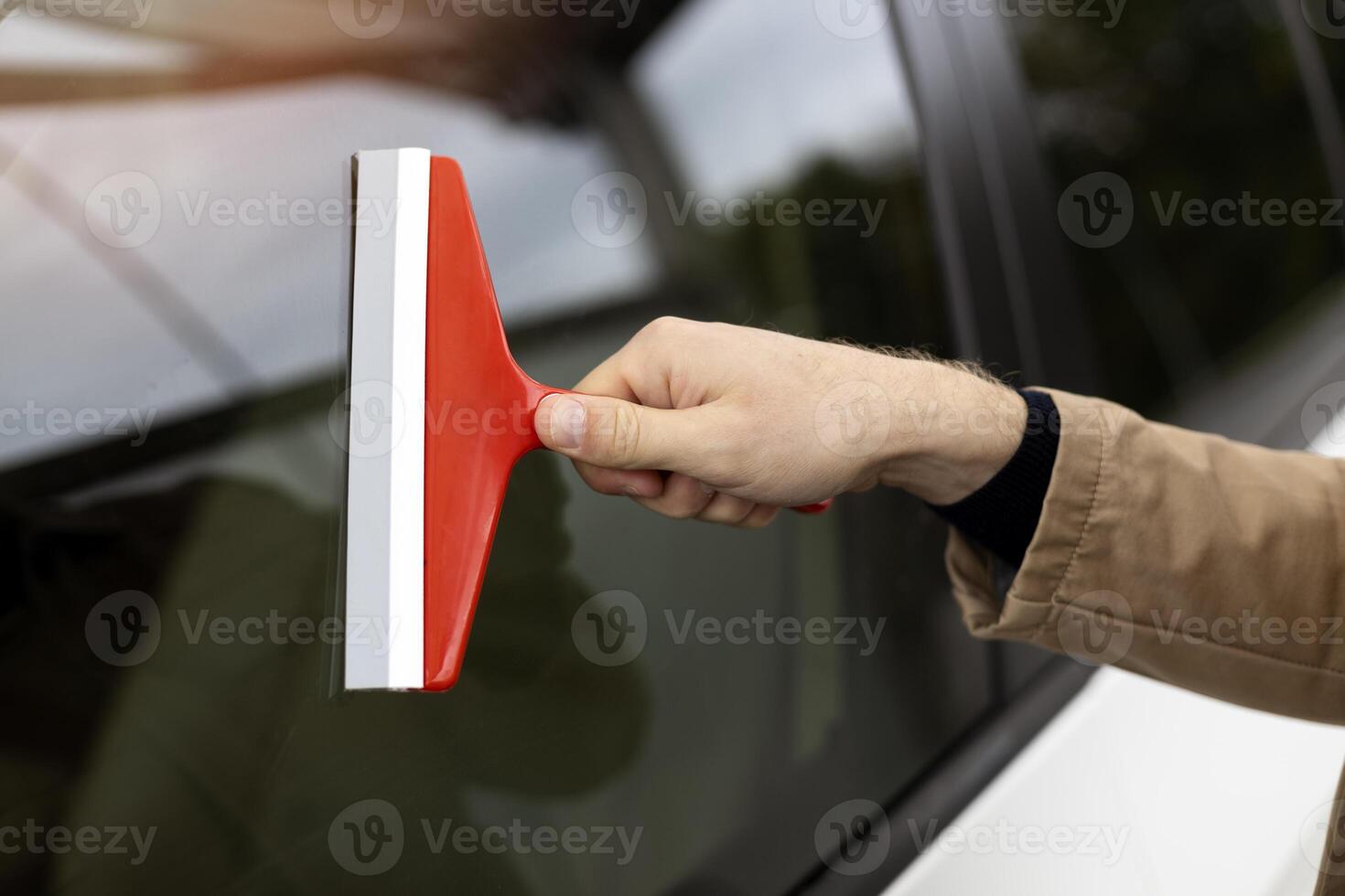 Man cleaning car window using red scraper photo
