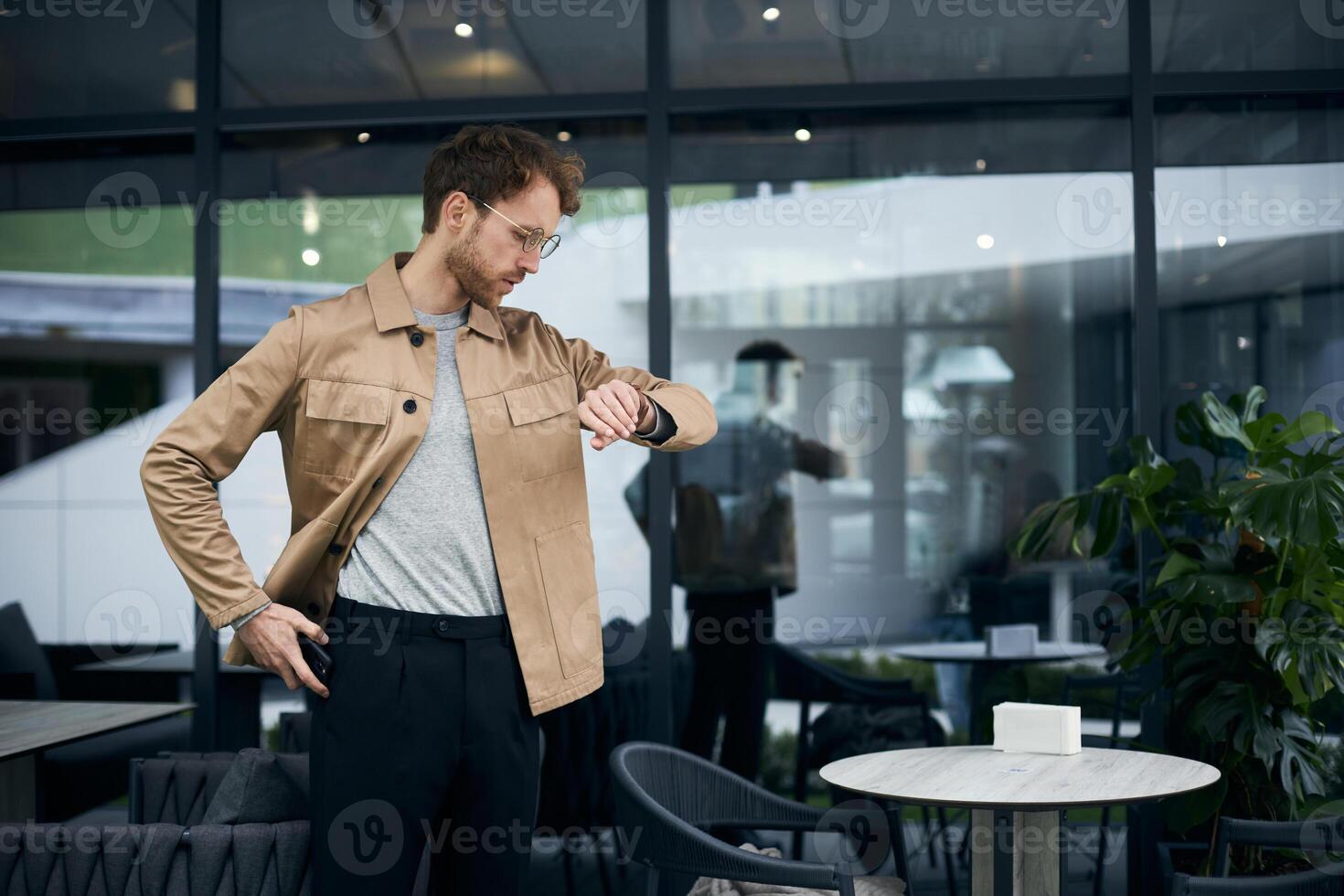 Stylish man checking time on wristwatch outside cafe photo