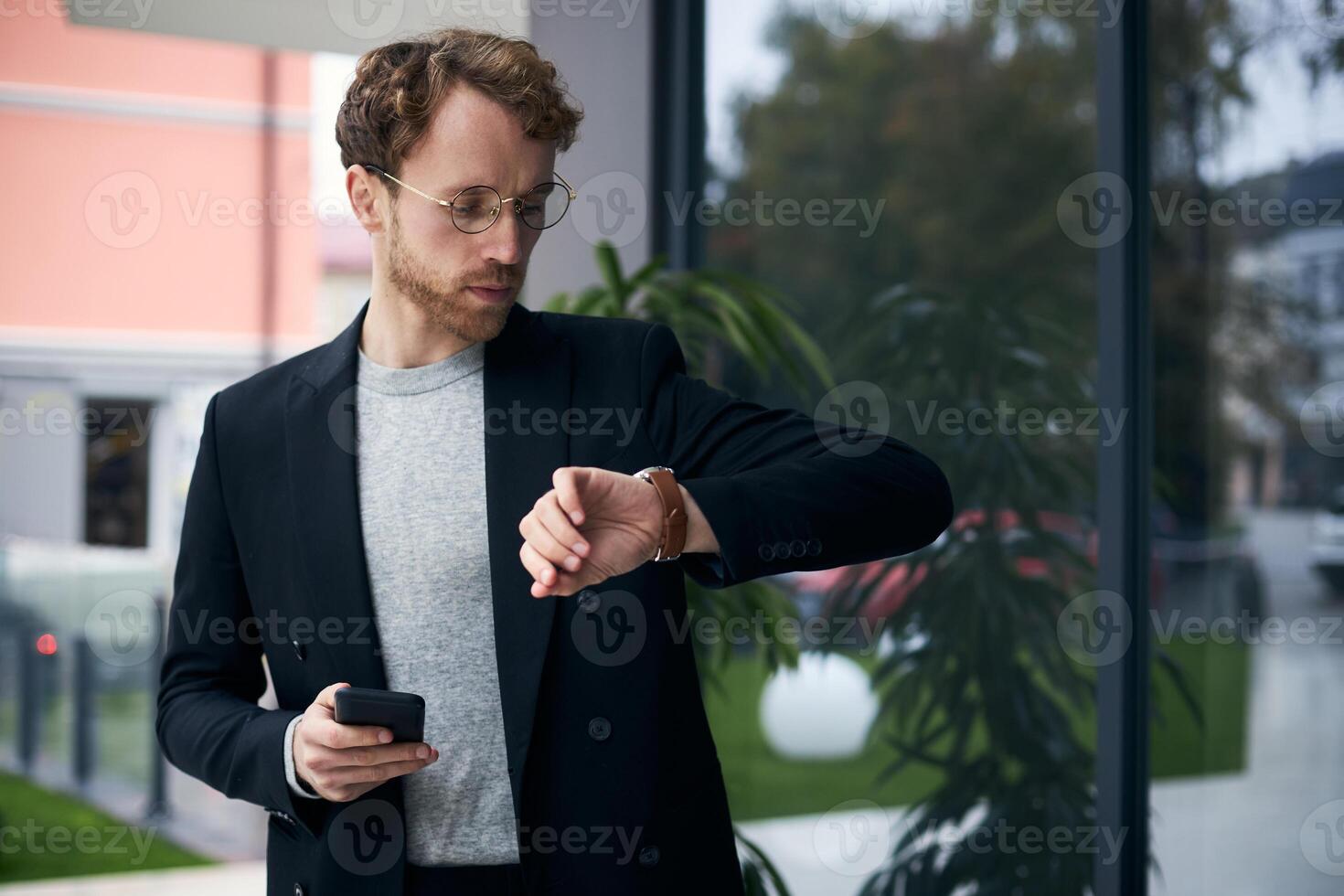 Businessman checking time on wristwatch holding smartphone photo