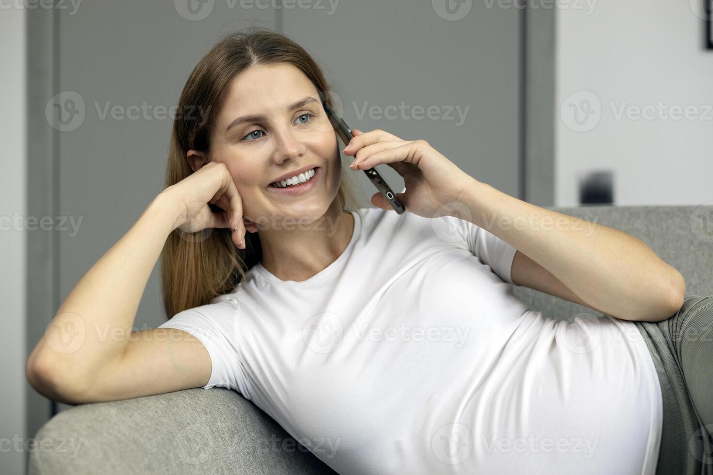Young woman relaxing on sofa is talking on smartphone photo