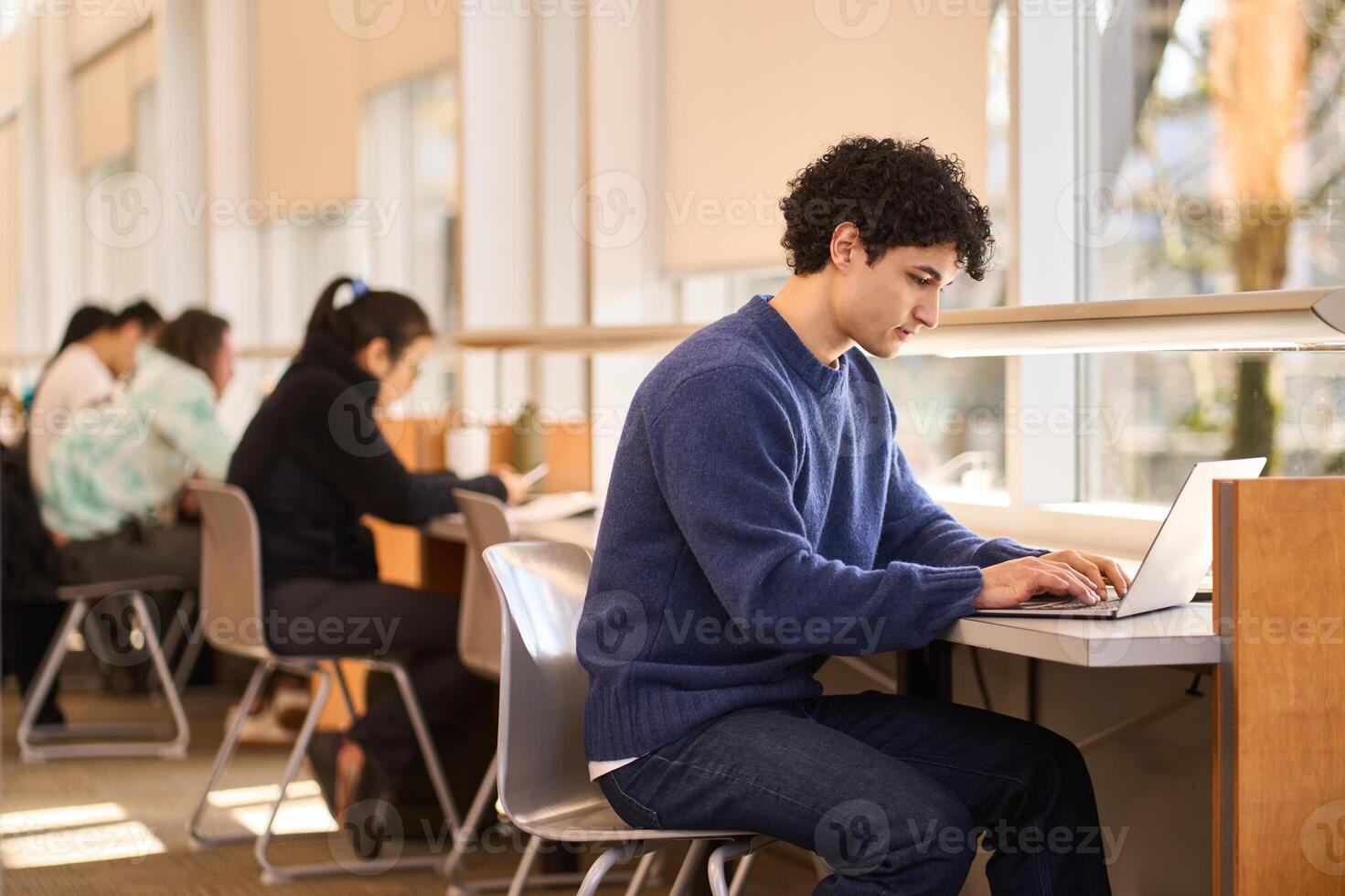 Focused student working on laptop in busy college library photo