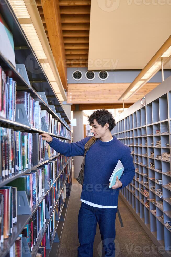 Young male student searching for book in college library photo