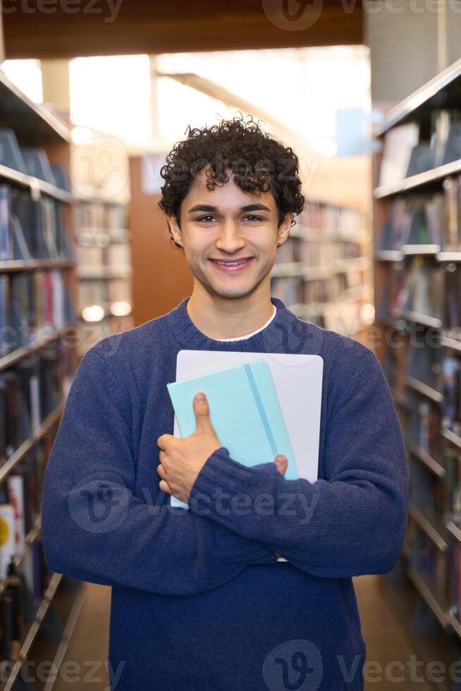 Happy college student holding books and laptop in library photo
