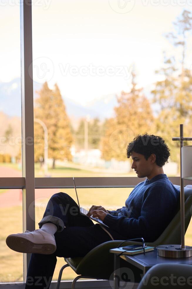 Young man working on laptop in modern office space with large windows photo
