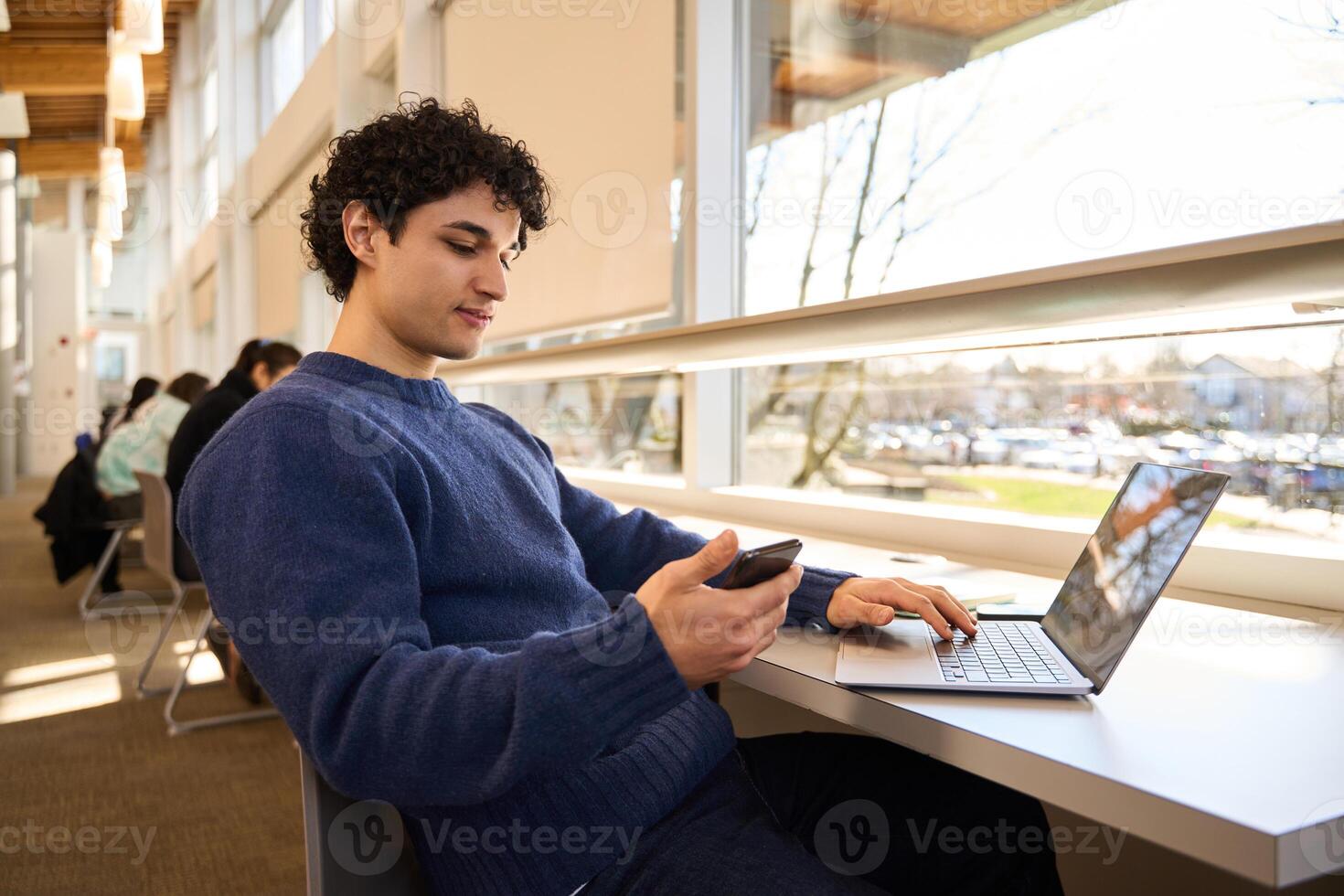 Focused student using laptop and smartphone studying in university library photo