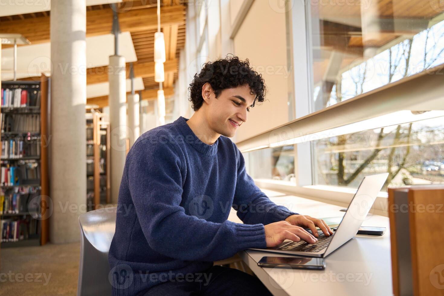 Smiling student working on laptop in university library photo