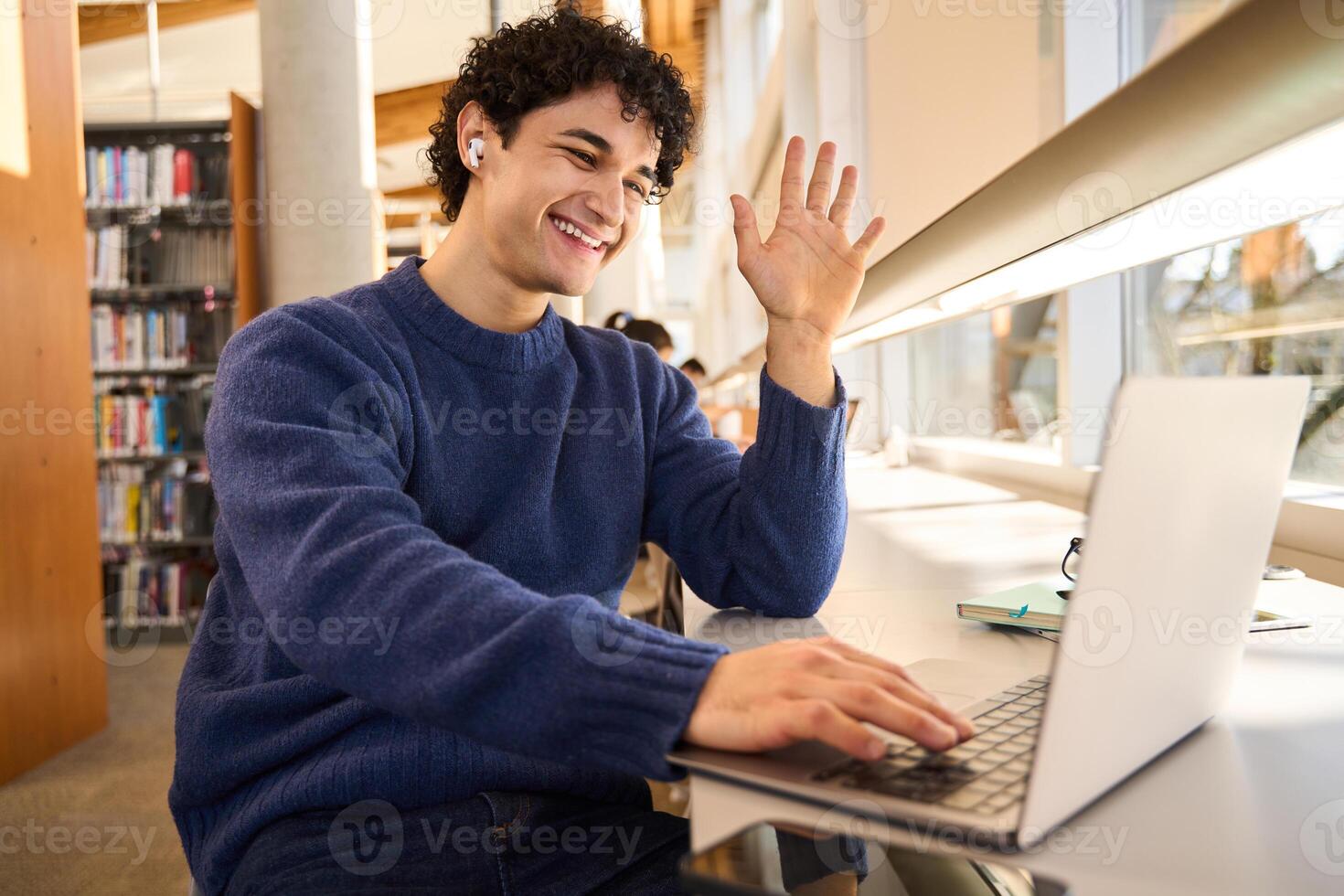 Happy student waving during call in library photo