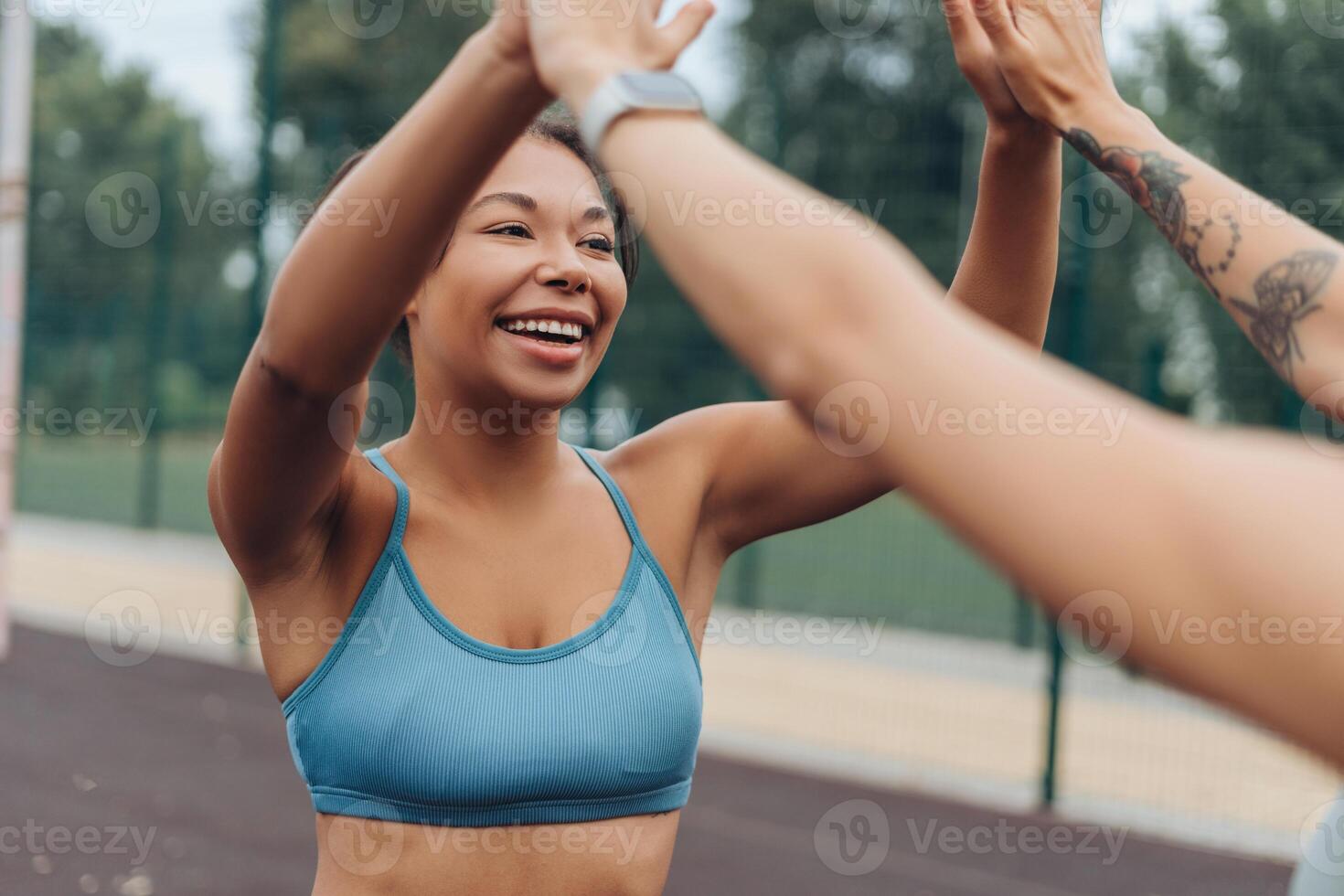 Excited, smiling, happy African American woman wearing stylish sportwear giving high five outdoors photo