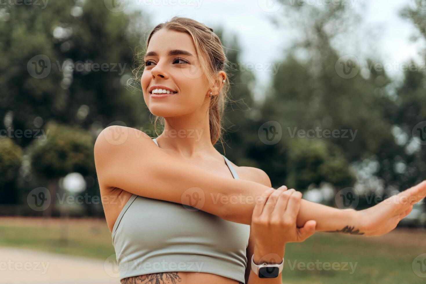 Smiling, beautiful woman wearing sport top warming up, stretching, looking away, doing exercise photo
