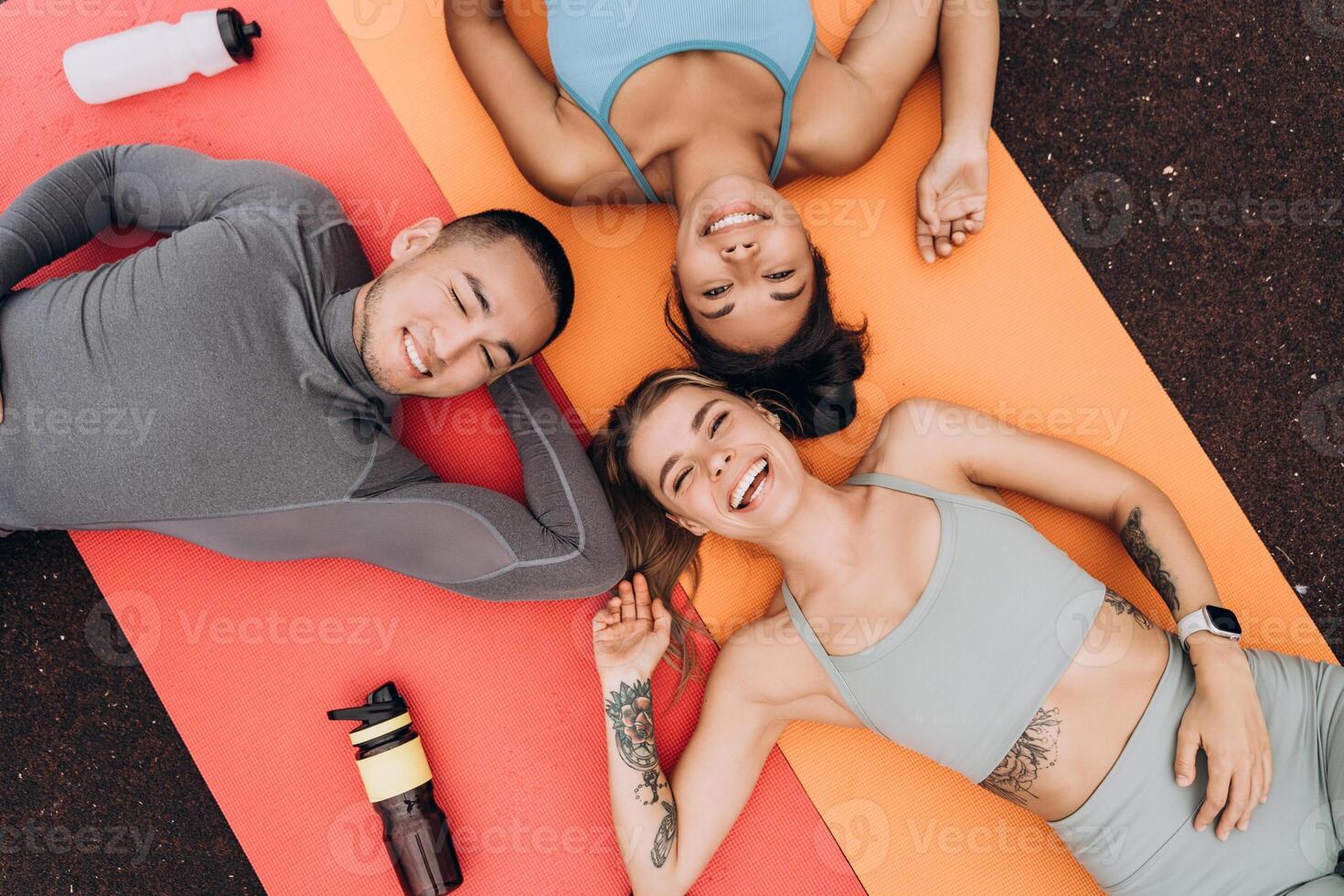 Happy, attractive sportspeople relaxing together, lying on sports mat, talking each other photo