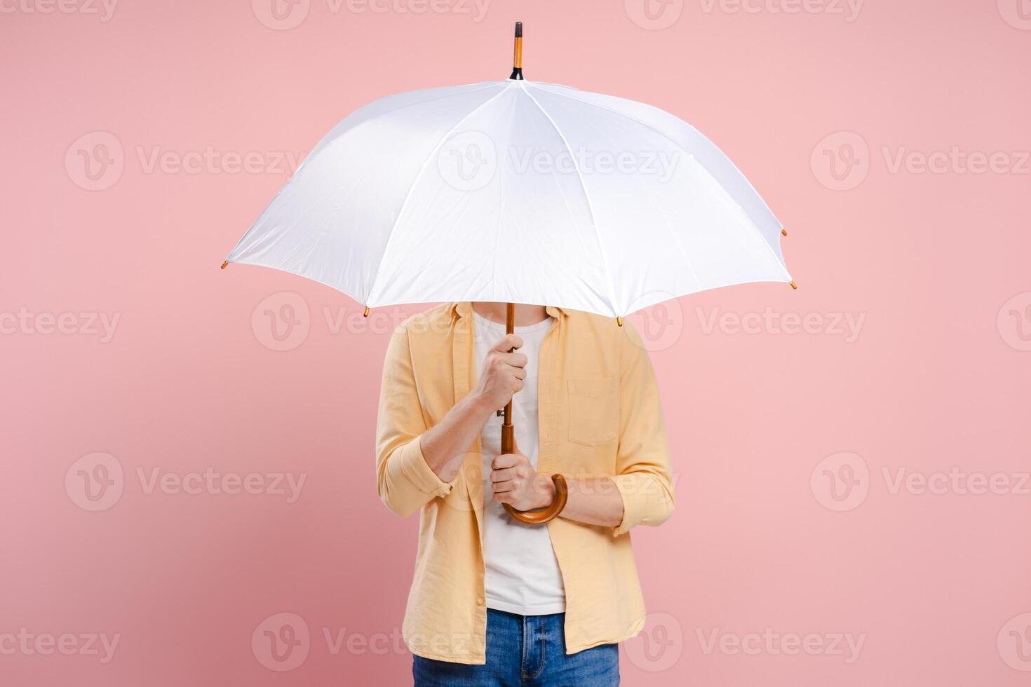 Young man hiding his face behind a white umbrella on a pink background photo