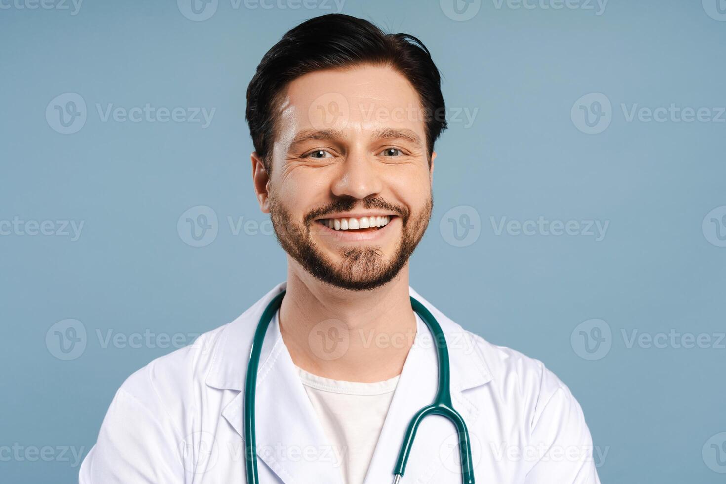 Portrait of smiling, friendly doctor posing wearing white coat isolated on blue background photo