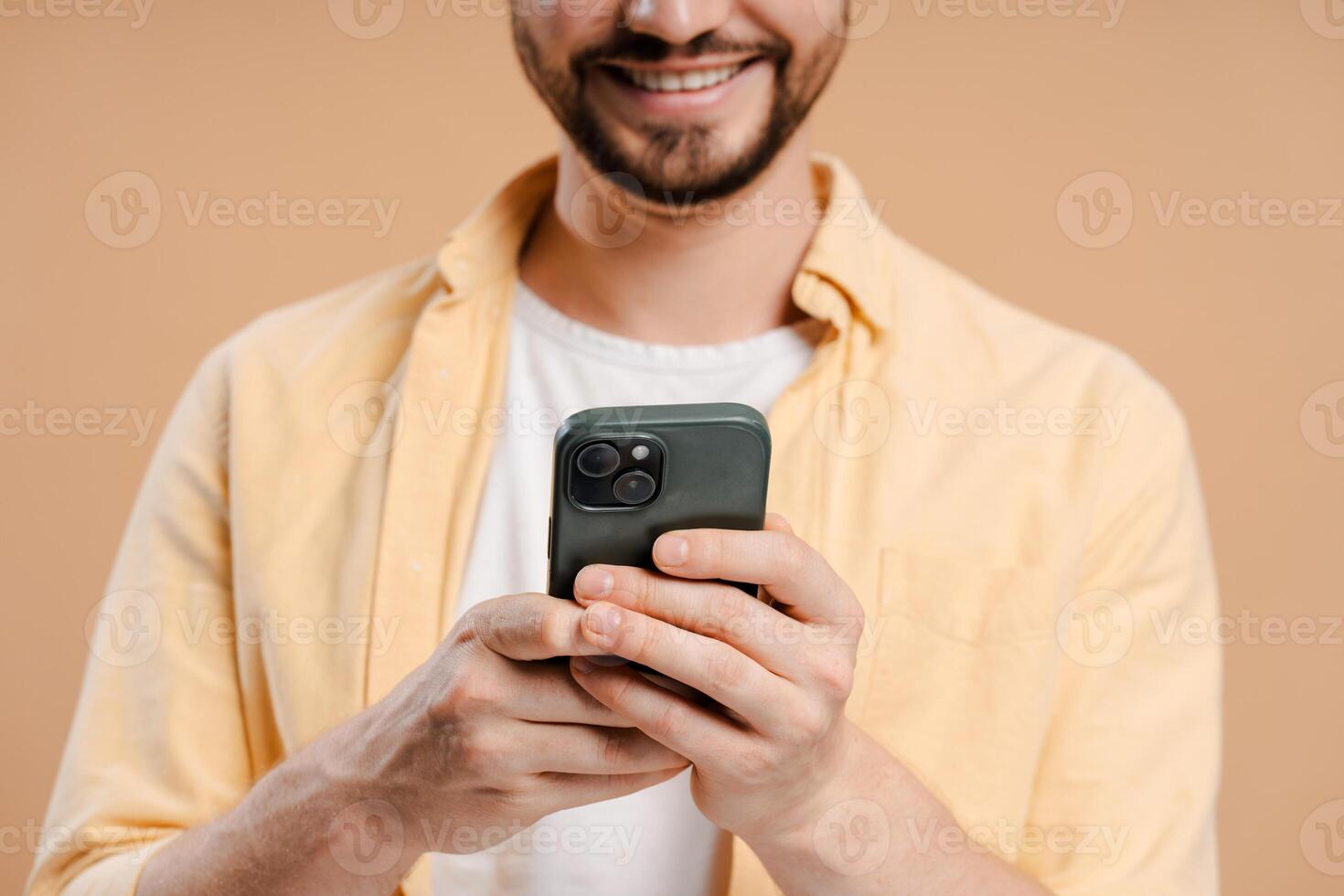 Bearded man holding using smartphone reading good news on social media isolated on beige background photo