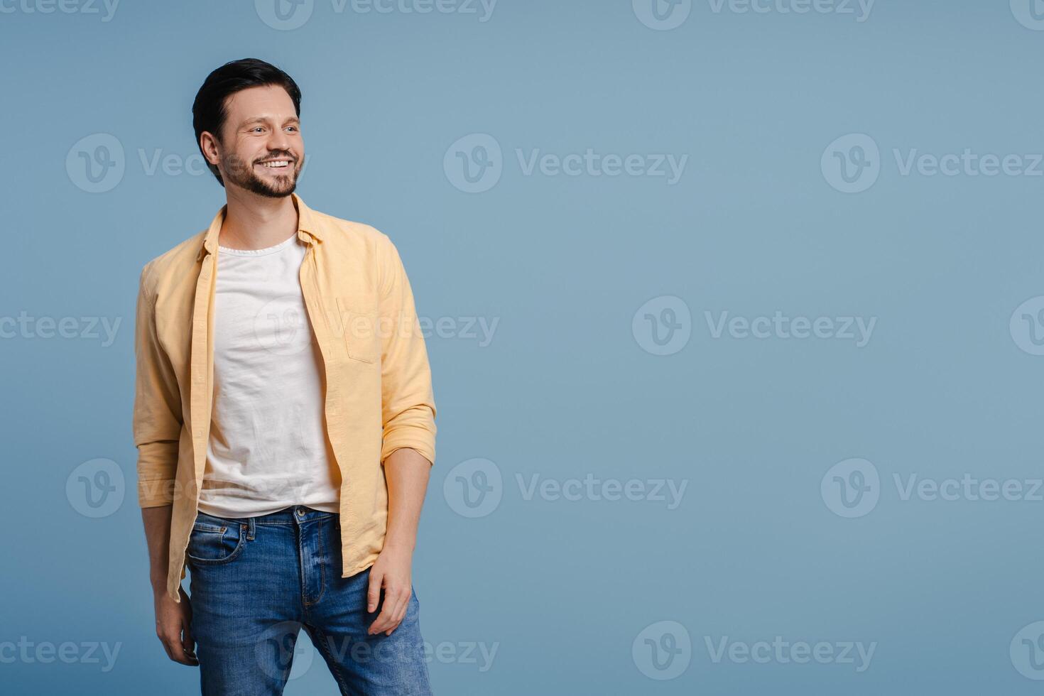 Handsome young man smiling and looking away on copy space on blue background photo