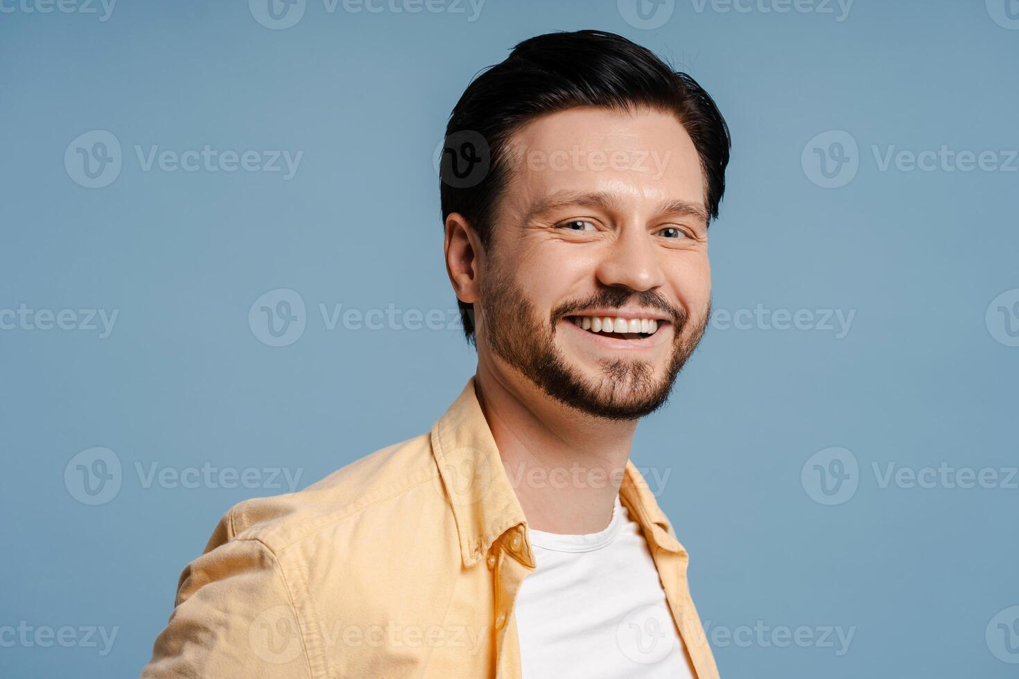 Cheerful young man with beard smiling and posing isolated on blue background photo