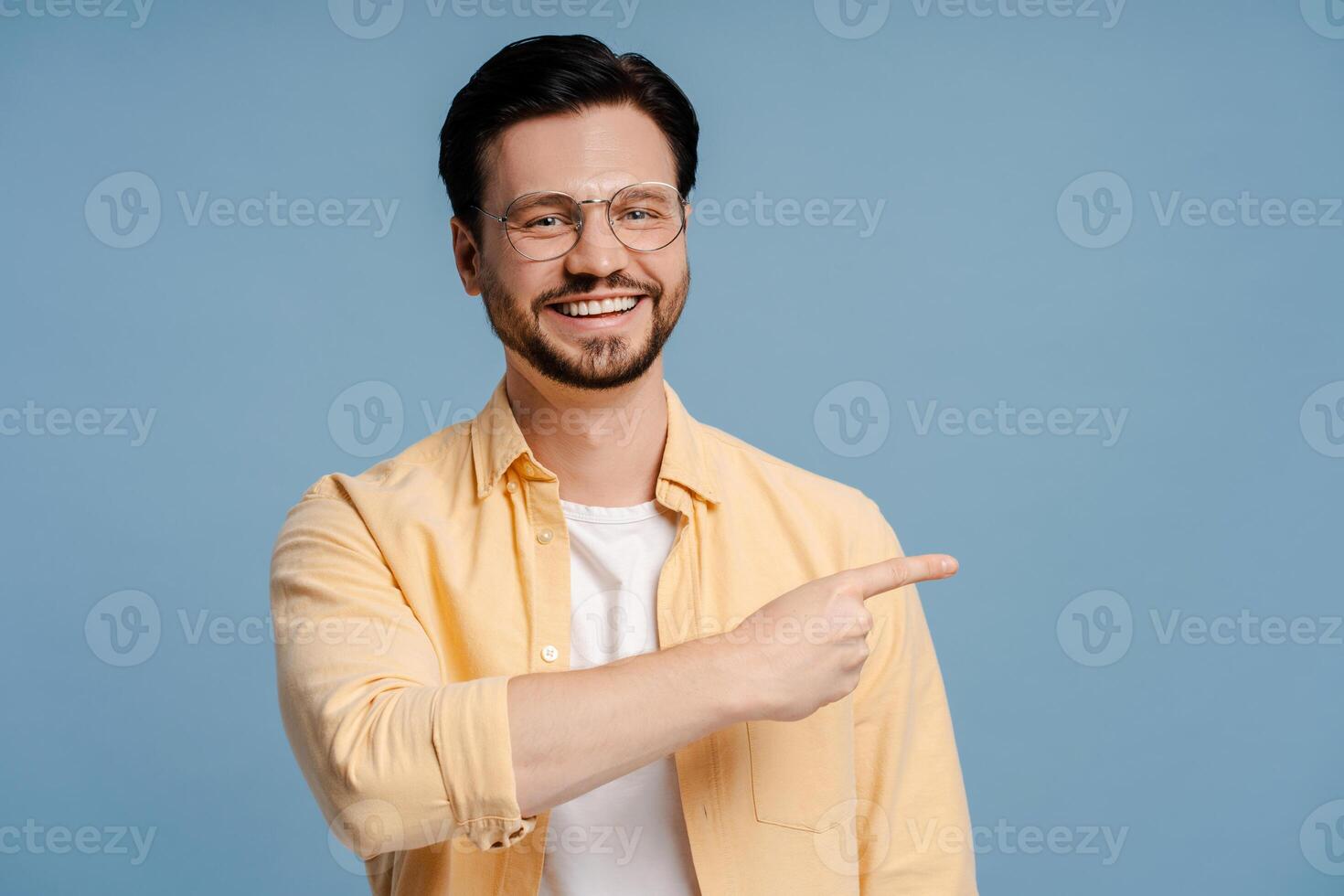 Cheerful man pointing aside while smiling on blue background photo