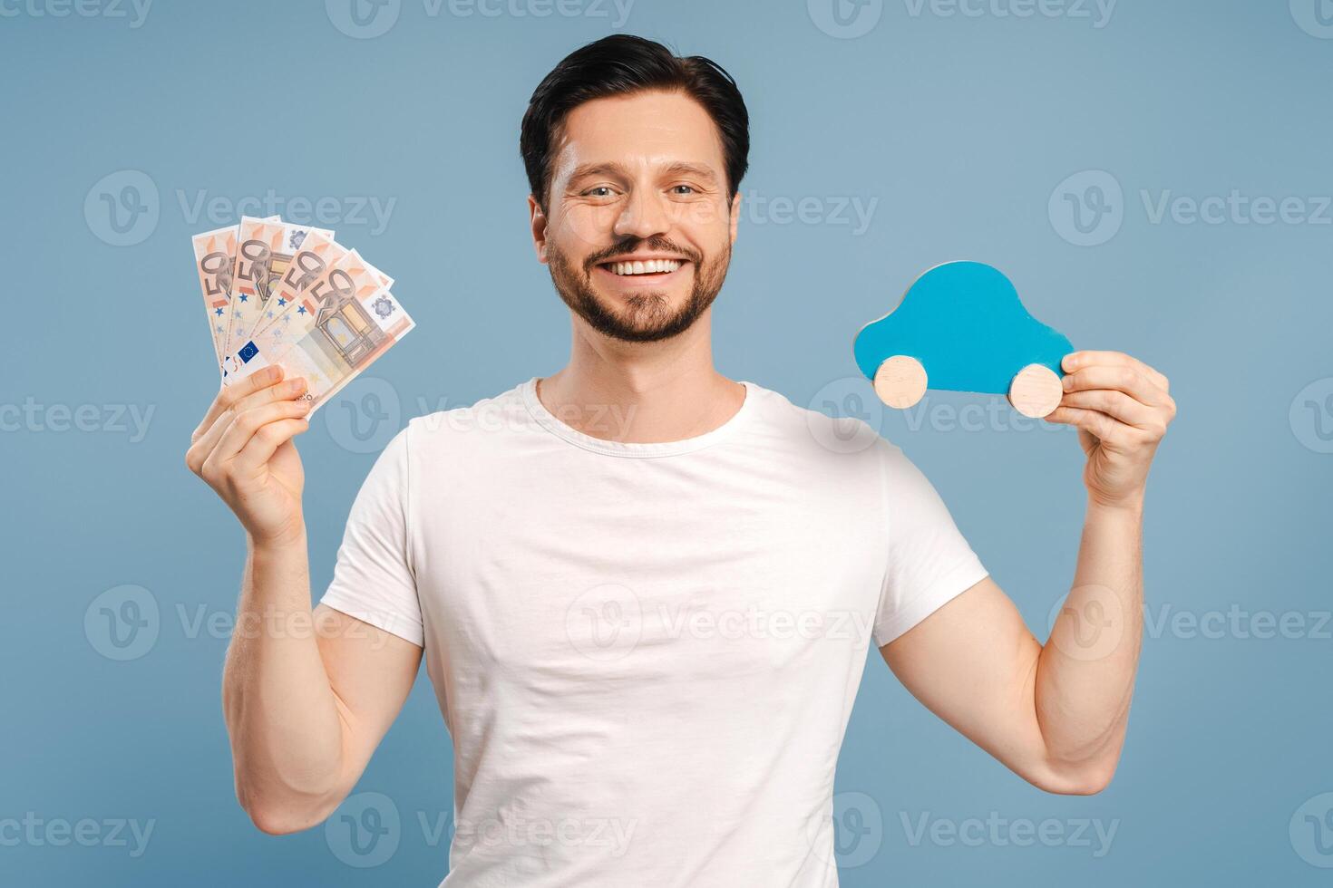Happy man holding euro banknotes and toy car for savings isolated on blue background photo