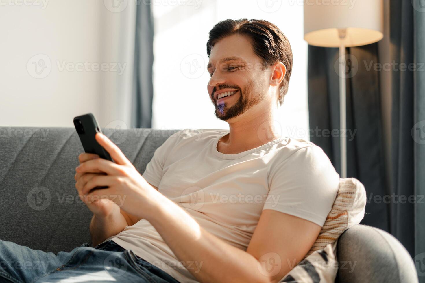 Happy man using smartphone relaxing on sofa at home photo