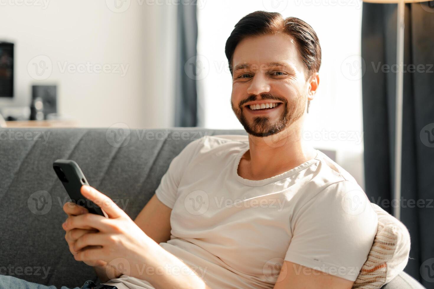 Happy man using smartphone relaxing on sofa at home photo