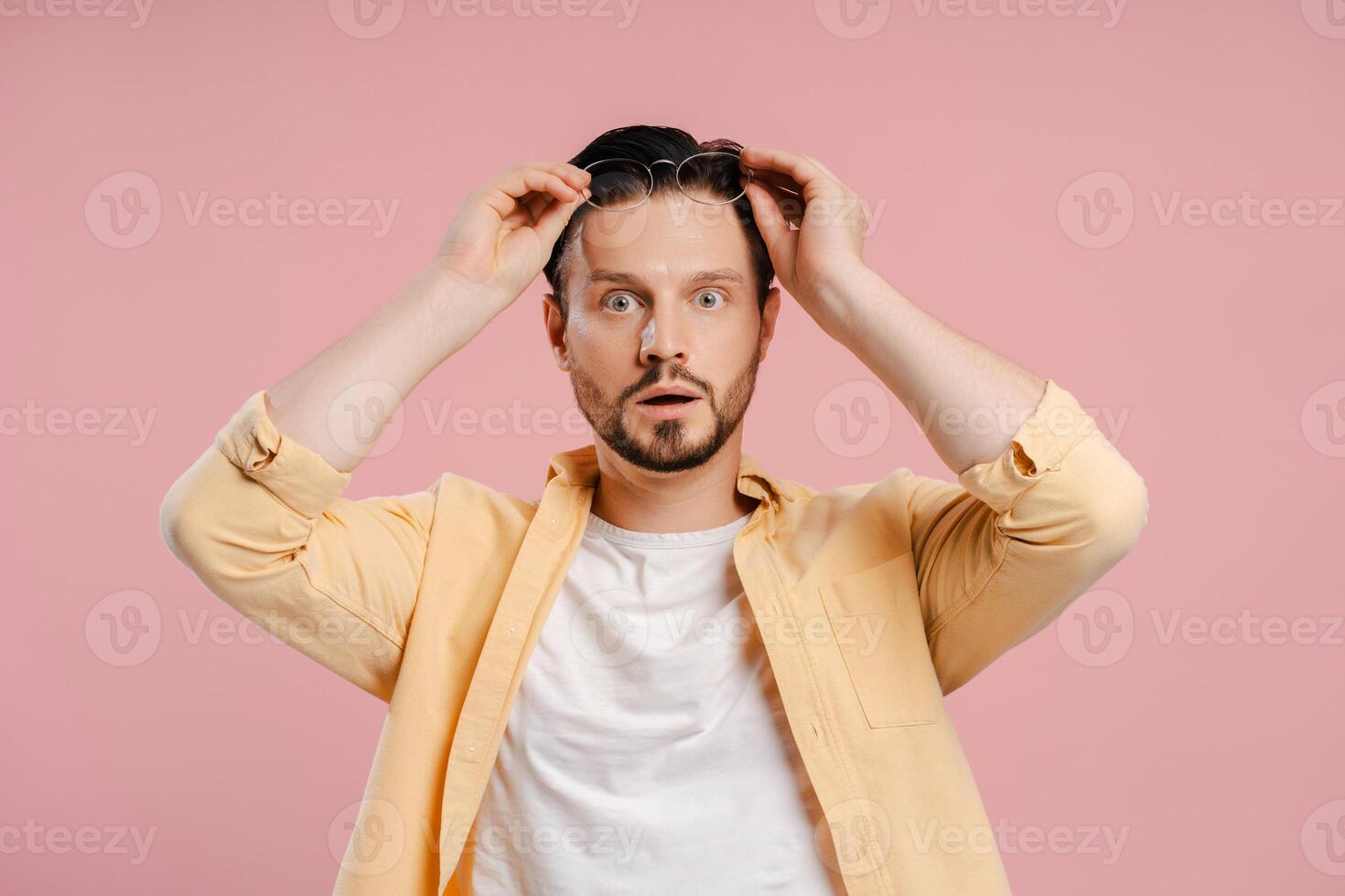 Shocked man adjusting glasses on pink background, looking at camera photo