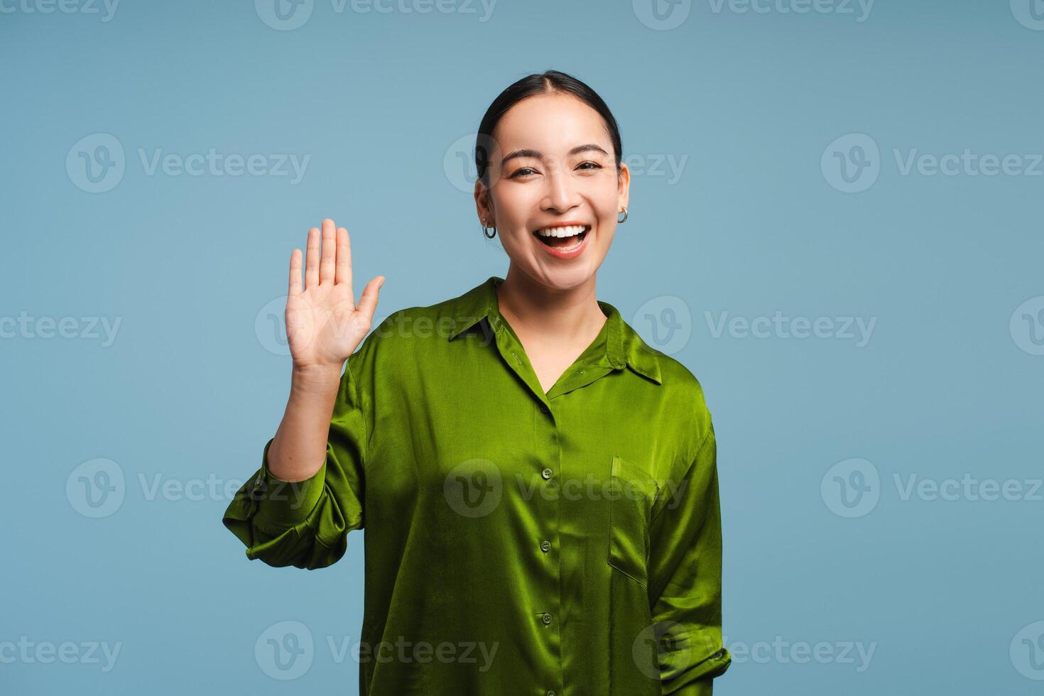 Young, happy Asian woman waving and smiling isolated on blue background photo