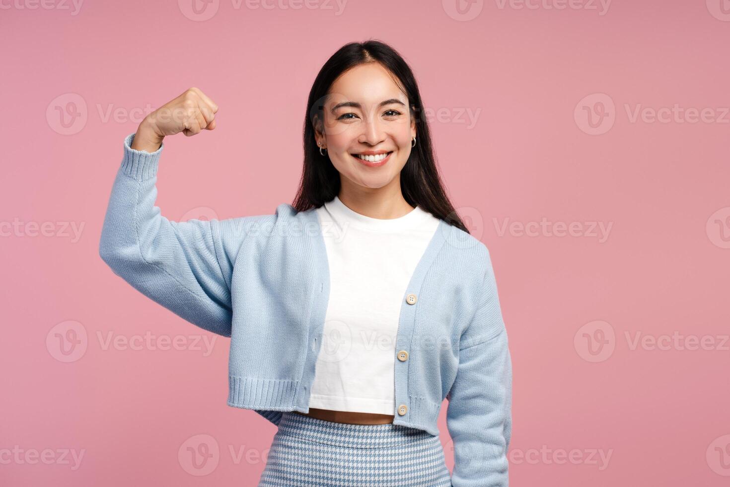Smiling, attractive Asian woman flexing muscles showing her strength on pink background photo