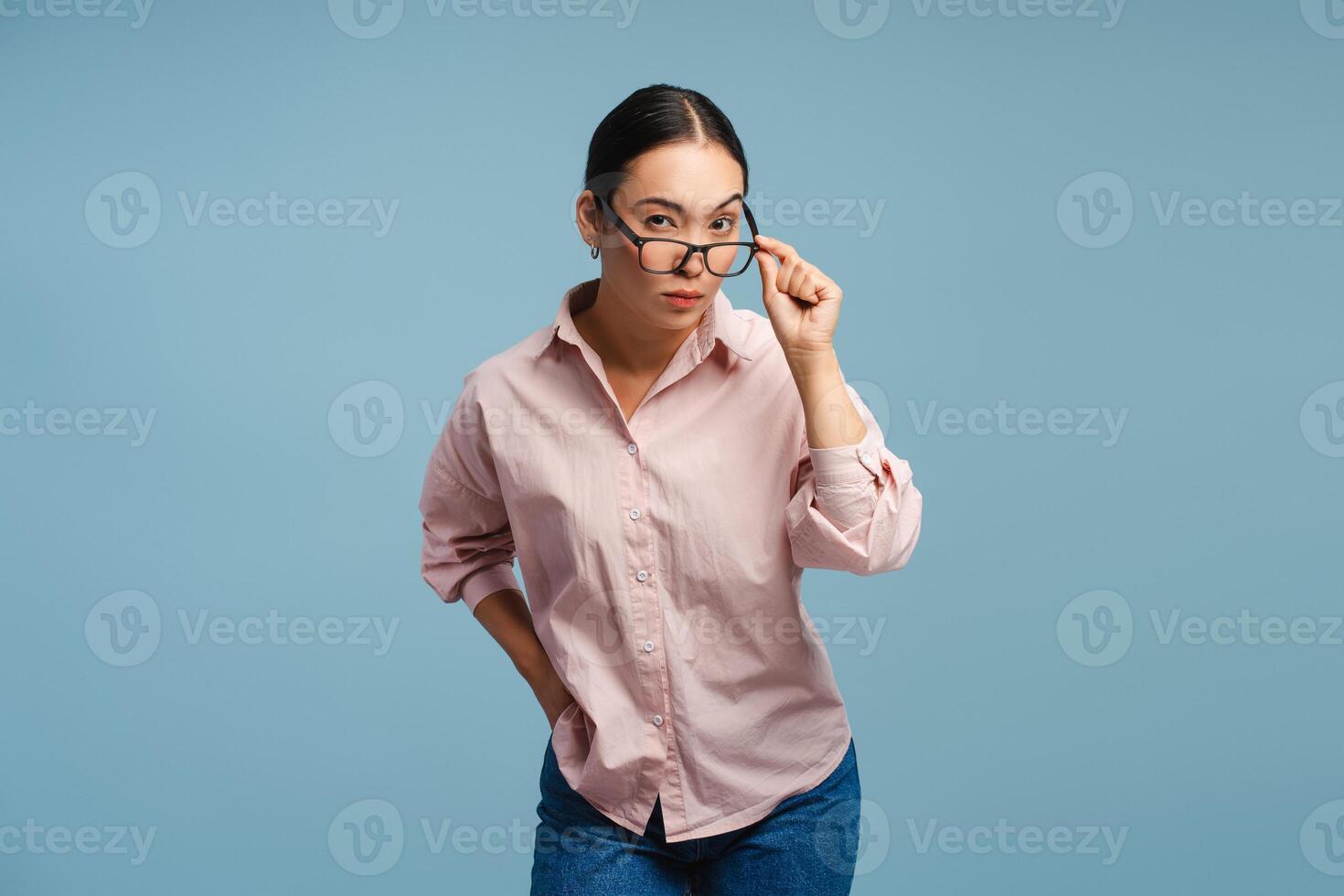 Serious, pensive Asian woman adjusting eyeglasses isolated on blue background photo