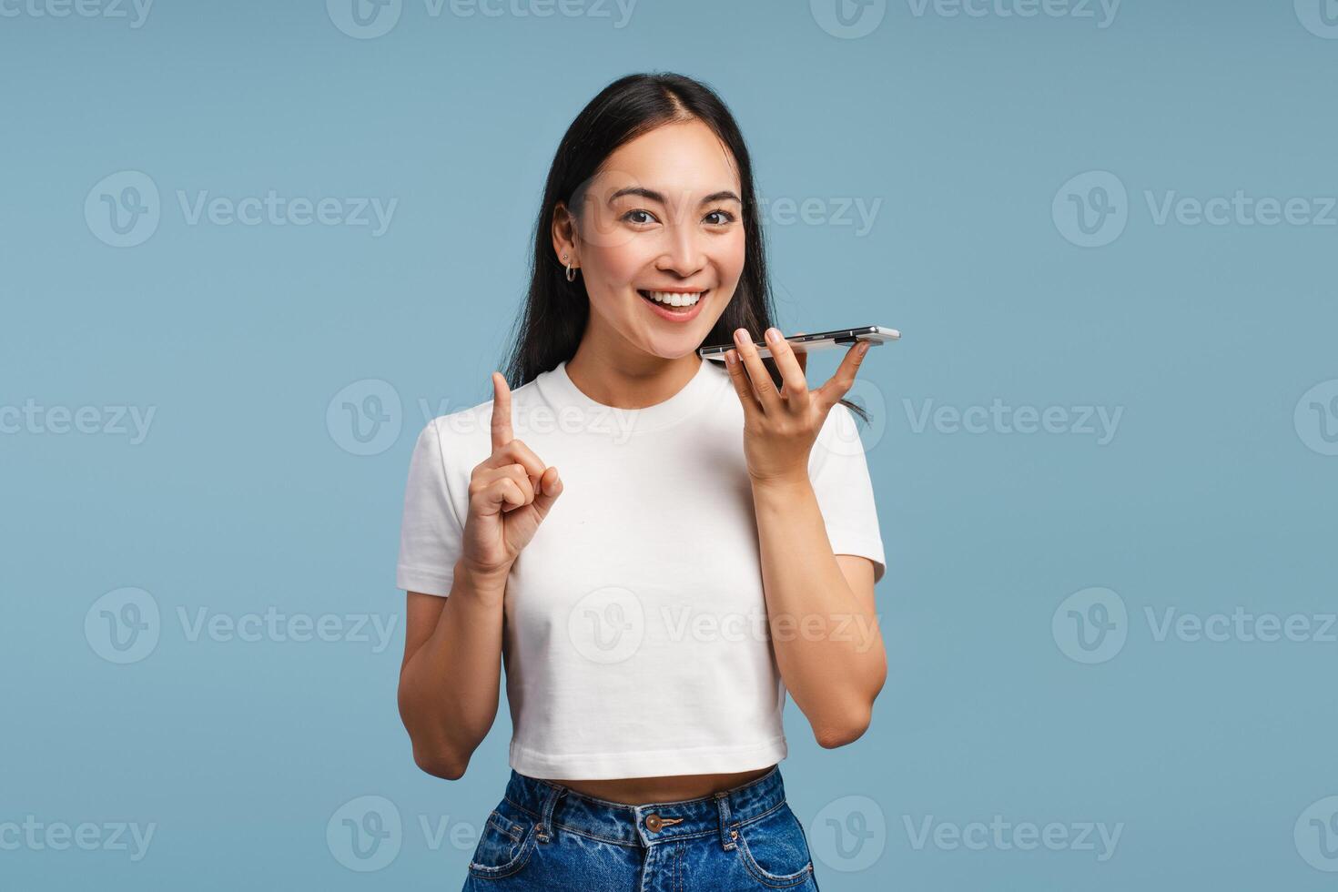 Attractive Asian woman talking on speakerphone and pointing index finger looking at camera photo