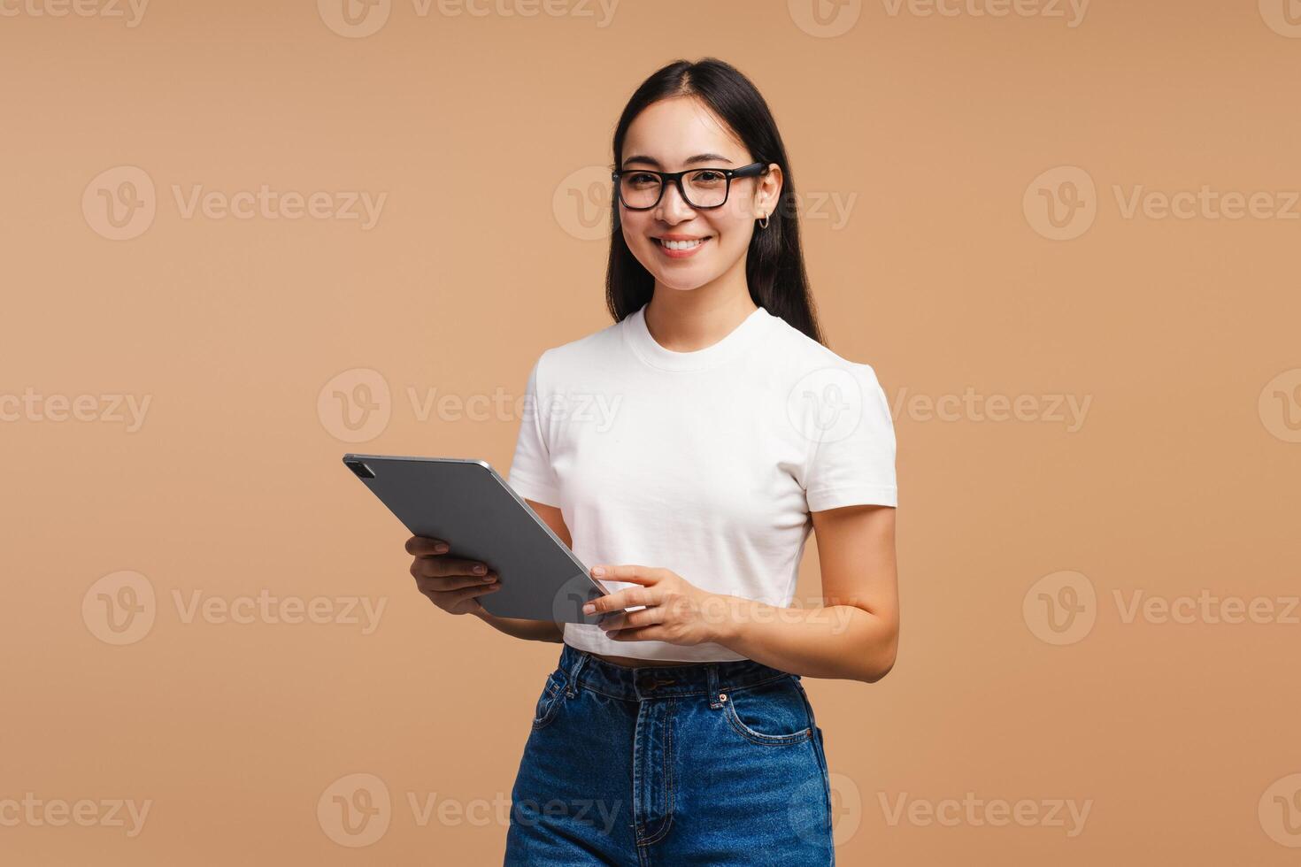 Young, attractive, Asian woman holding digital tablet smiling, looking at camera on beige background photo