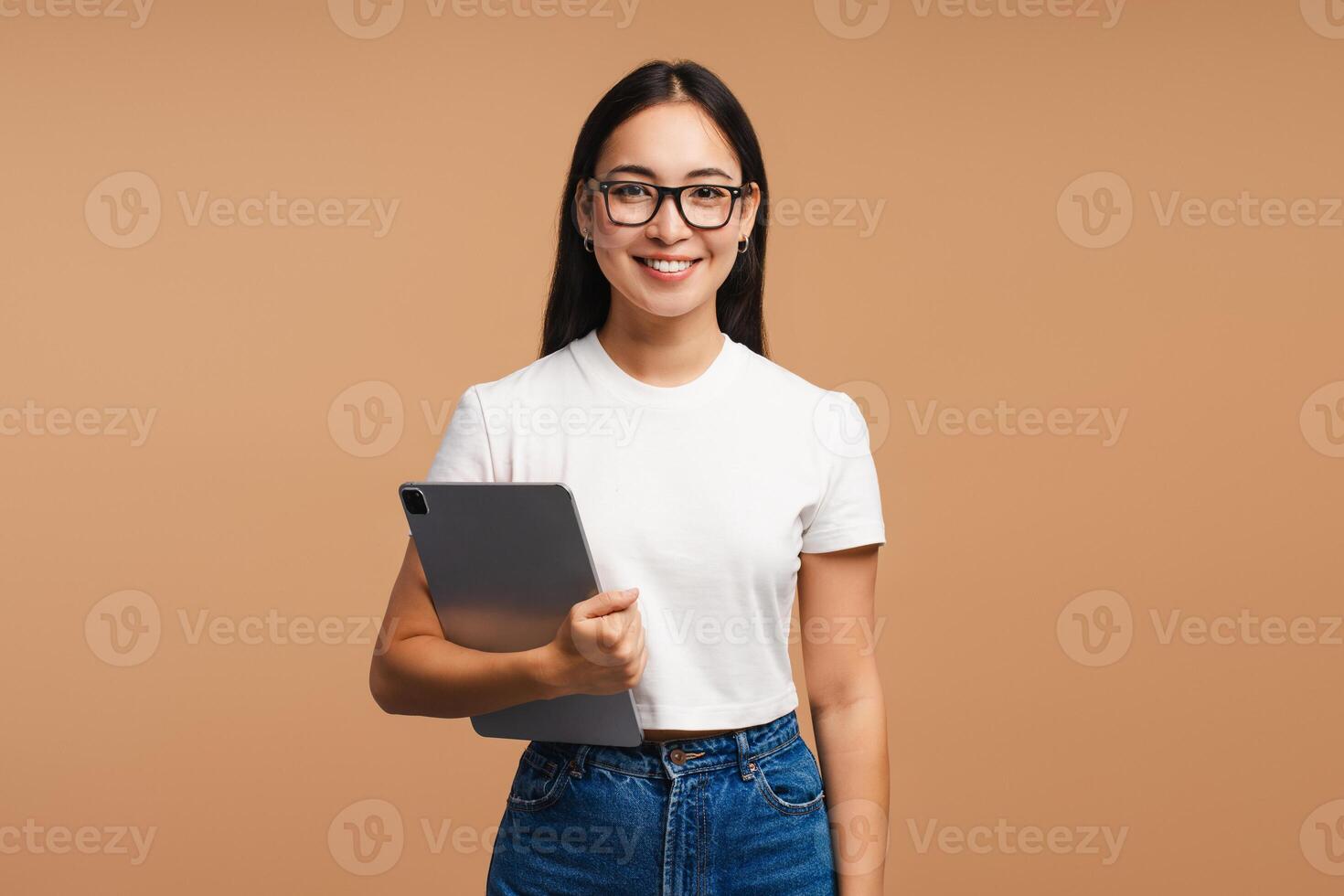 Asian woman wearing eyeglasses holding digital tablet looking at camera isolated on beige background photo