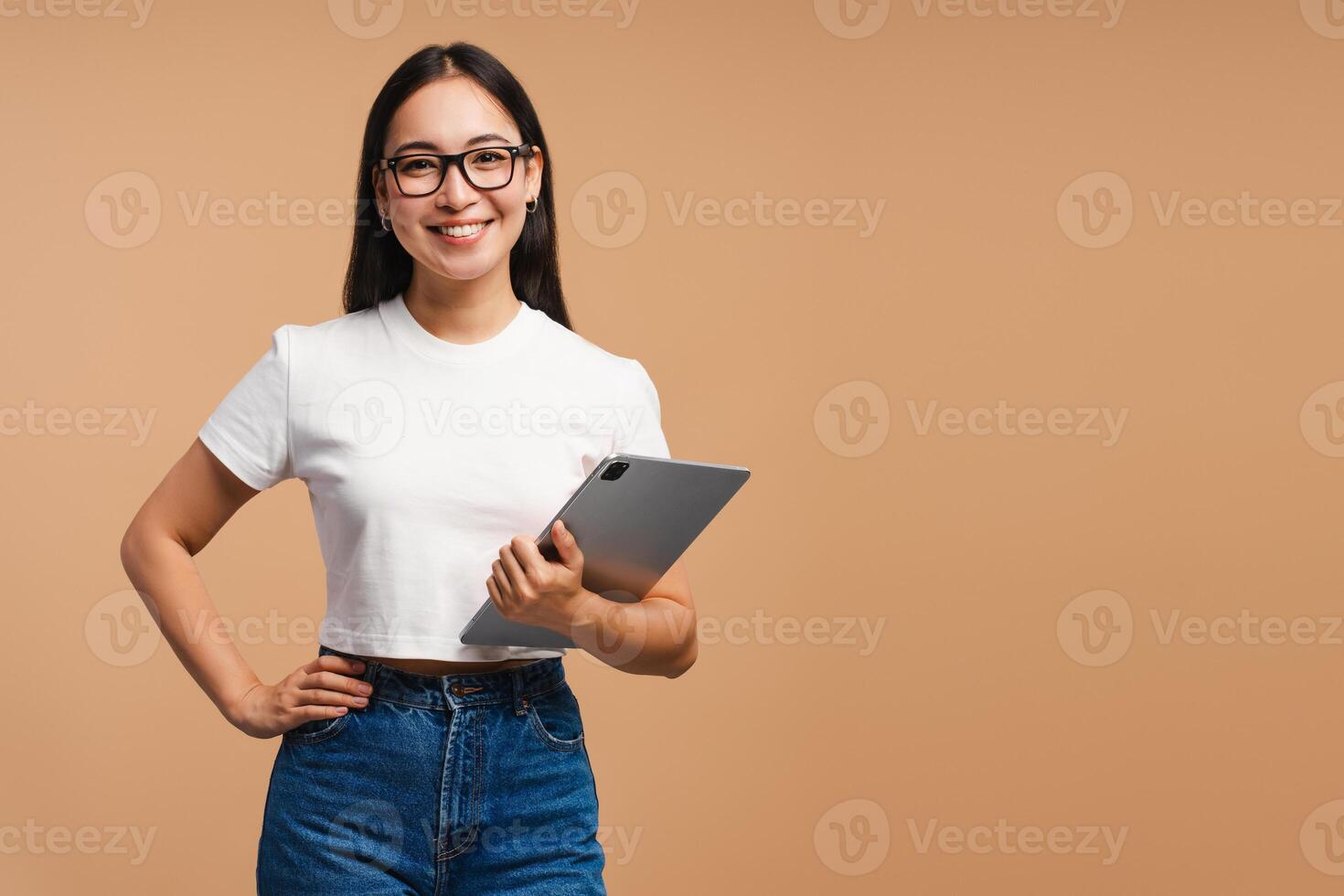 Smiling, Asian woman holding digital tablet looking at camera, copy space on beige background photo