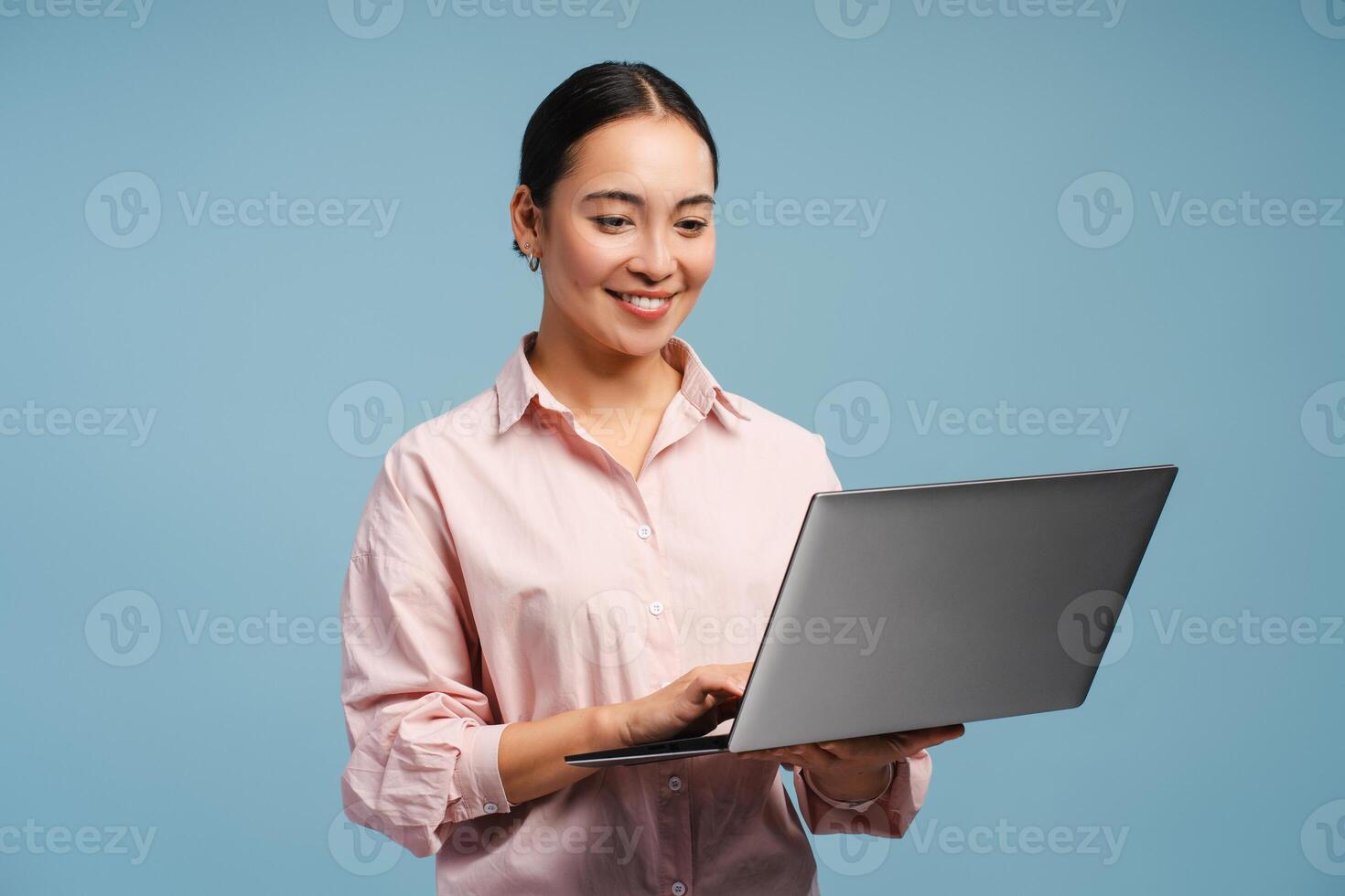 Attractive smiling professional Asian woman smiling and typing on laptop isolated on blue background photo