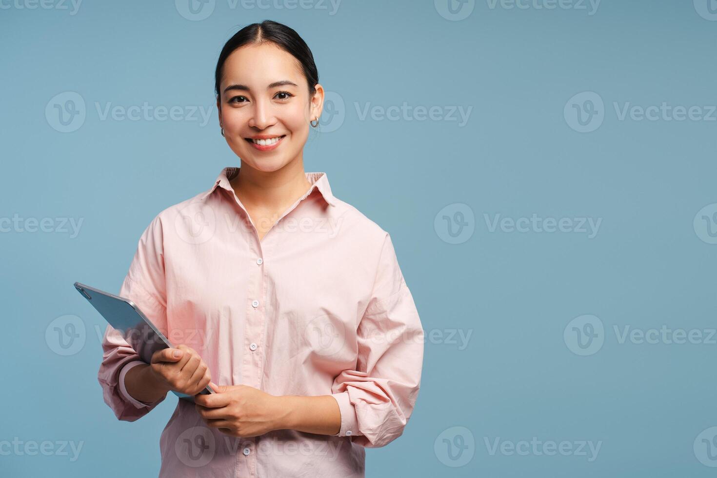 Smiling Asian businesswoman holding digital tablet smiling, looking at camera on blue background photo