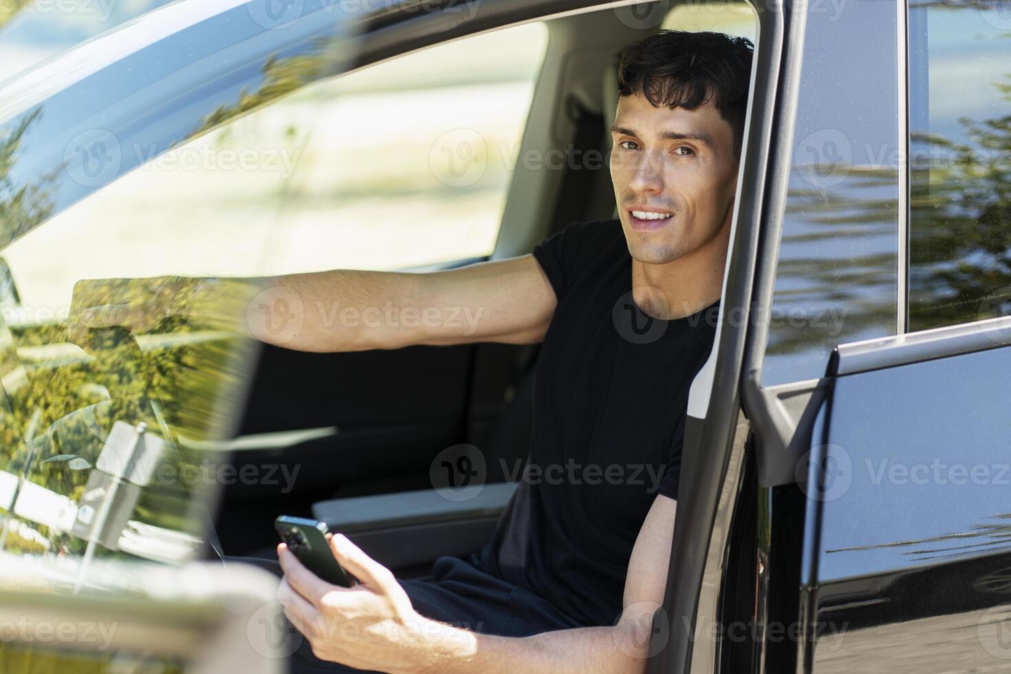 Young man holding steering wheel and using smartphone while sitting in car photo