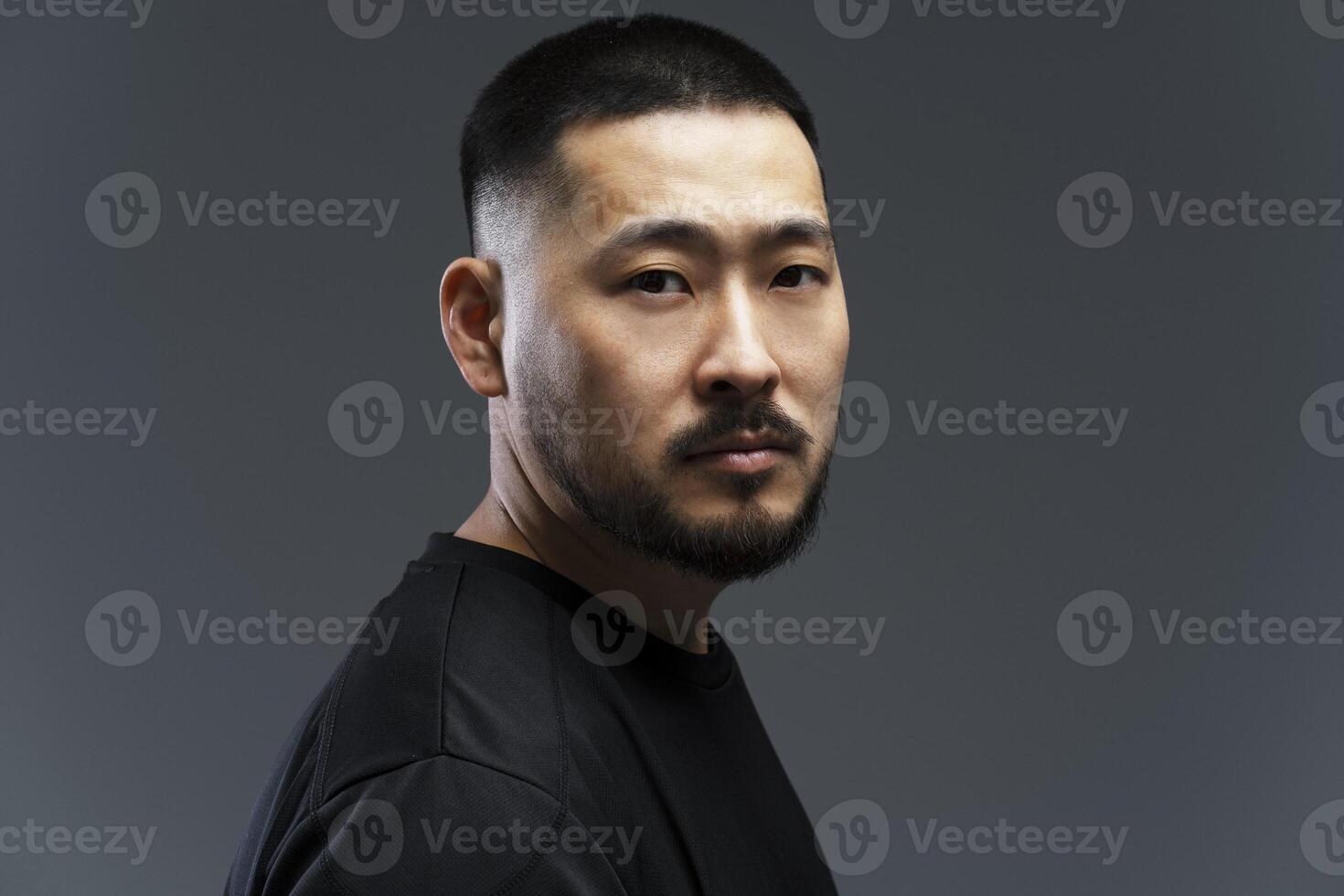 Serious asian man with black short hair and beard looking over shoulder photo