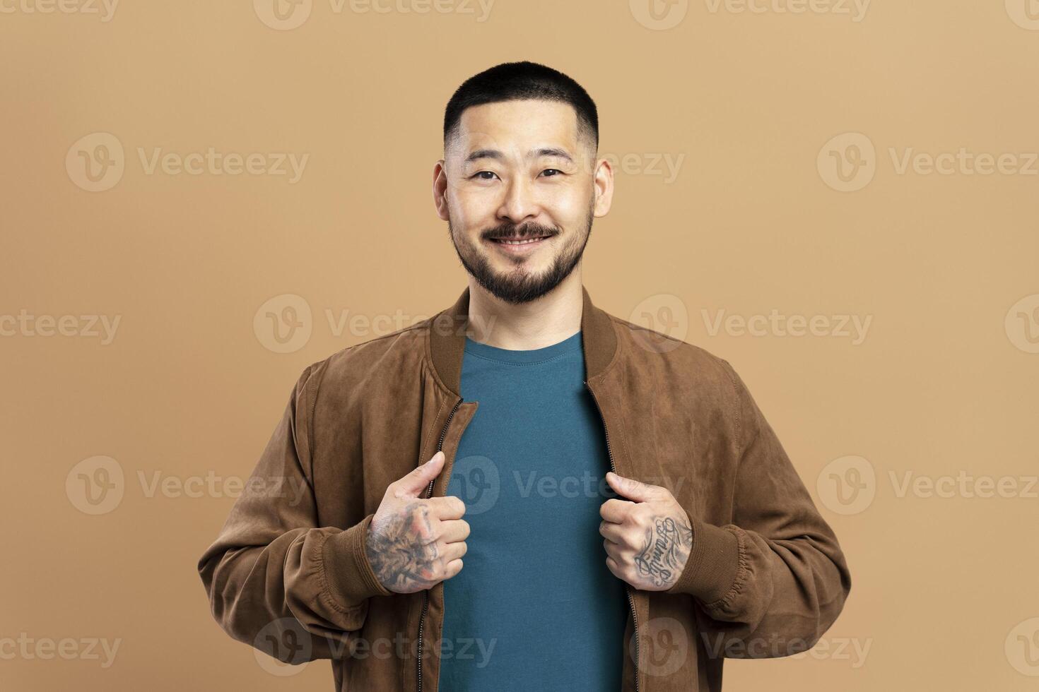 Smiling asian man with tattoos showing clothes is posing in studio photo