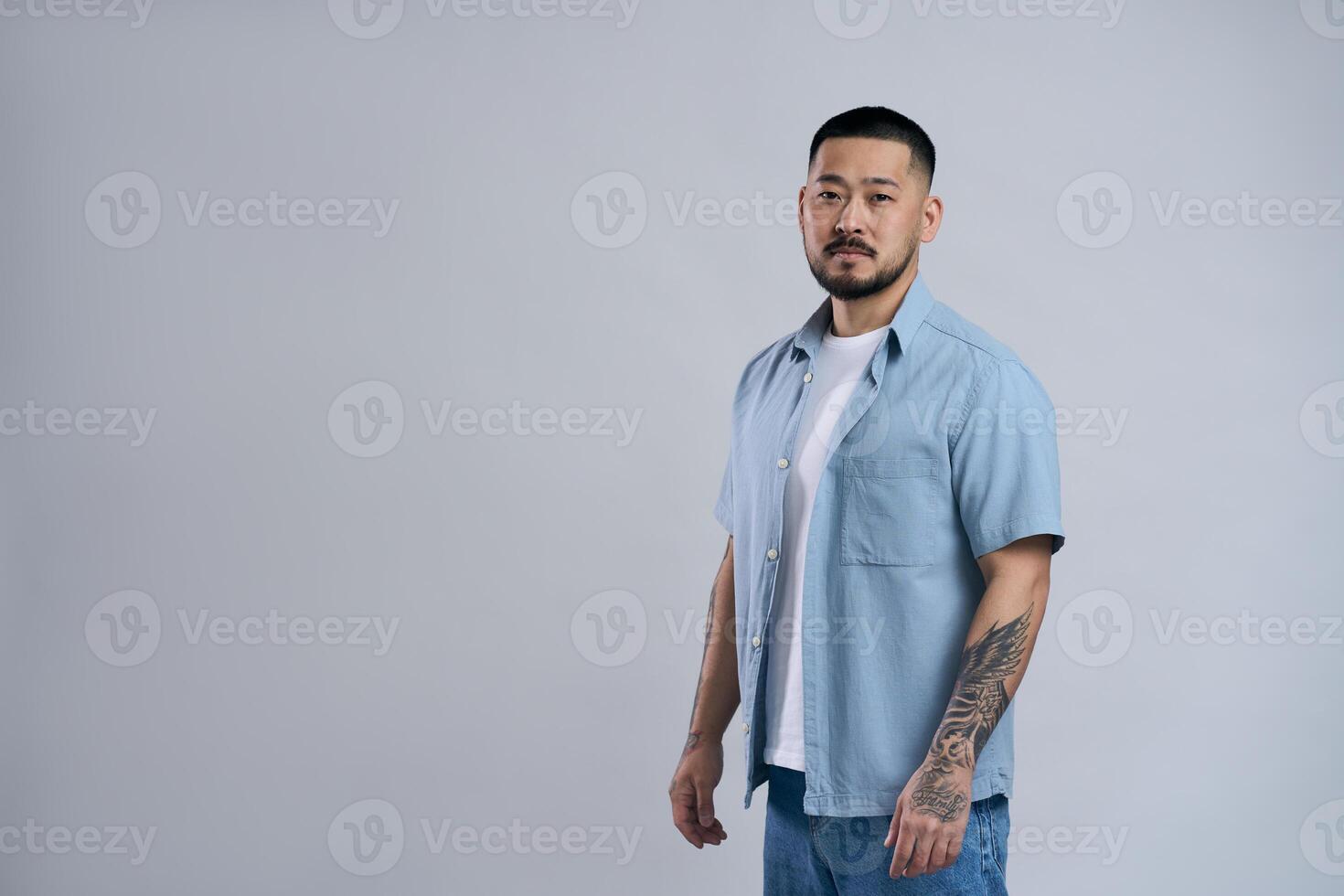 Serious young asian man with tattoos posing in studio photo