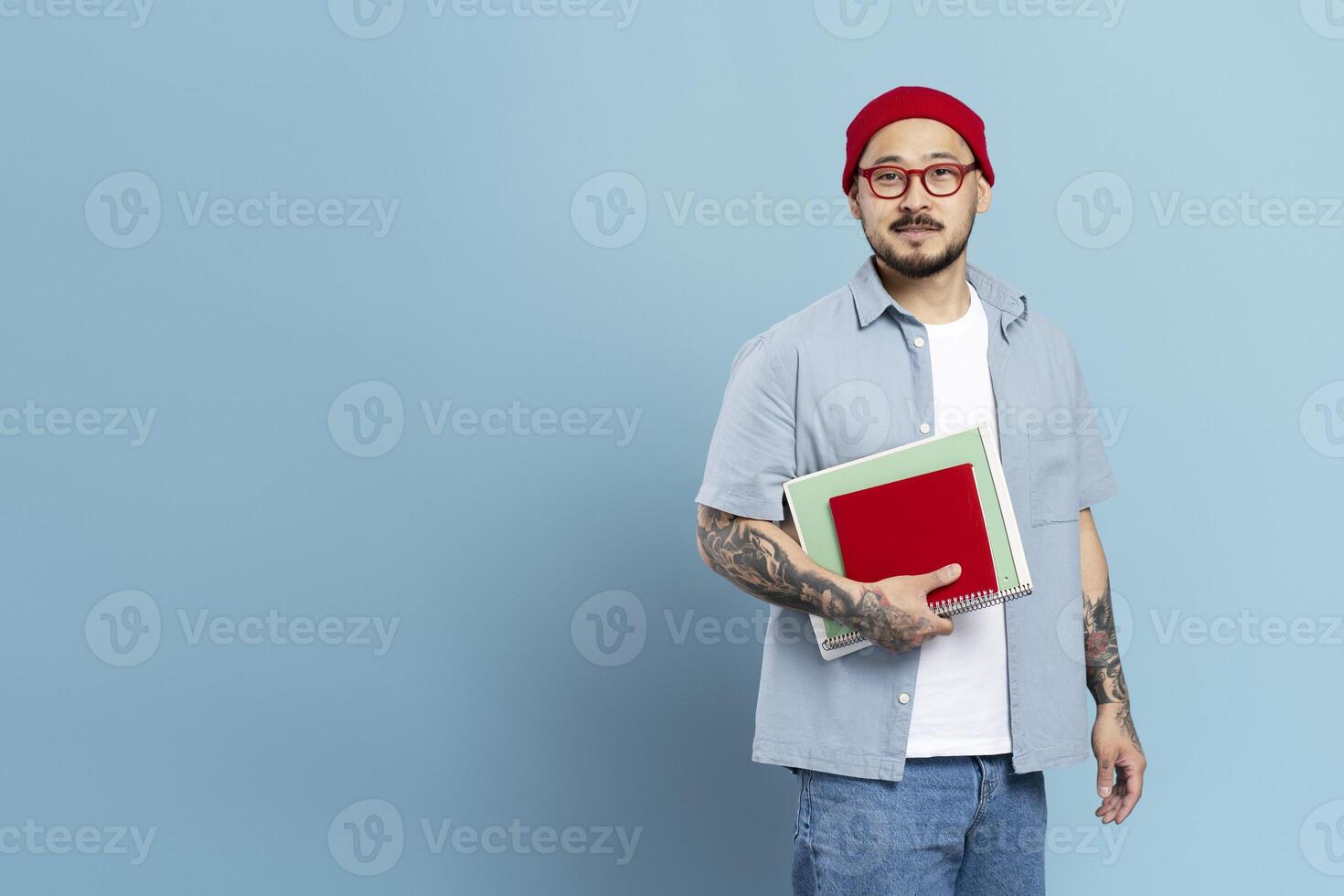 Confident tattooed student holding books on blue background photo