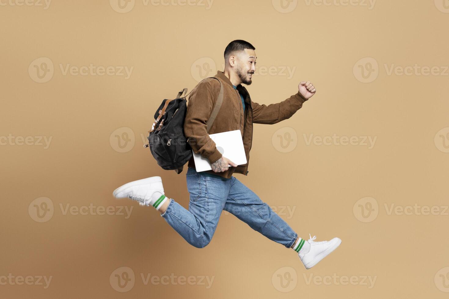 Young student running and jumping with laptop and backpack photo