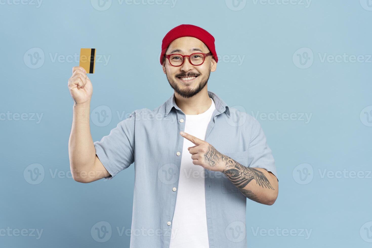 Smiling man showing credit card and pointing at it on blue background photo