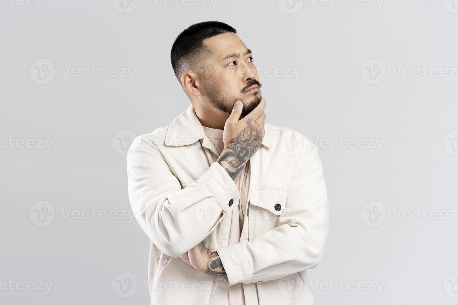 Thoughtful young man touching chin looking up on white background photo