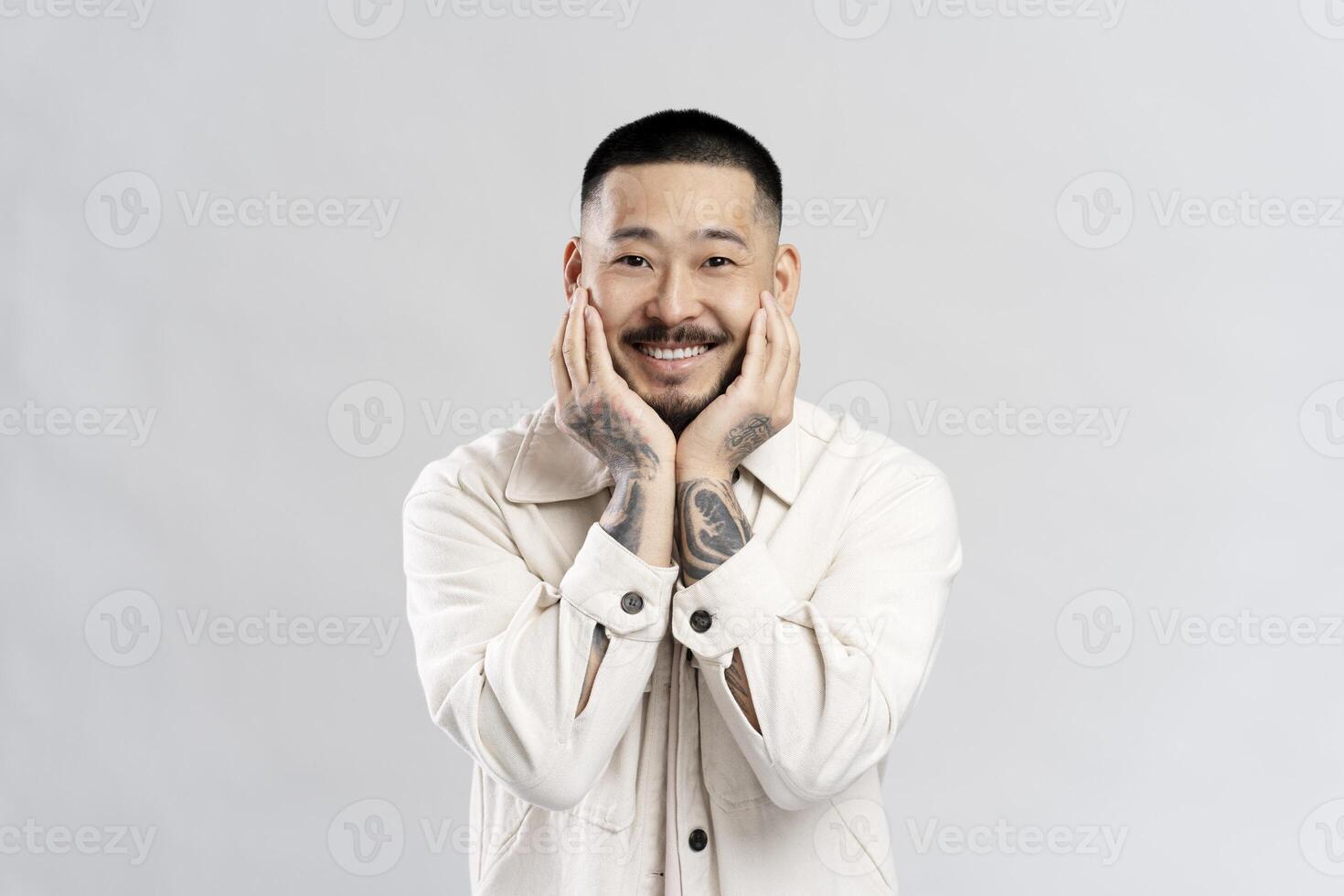 Young man with tattoos smiling and holding his face photo