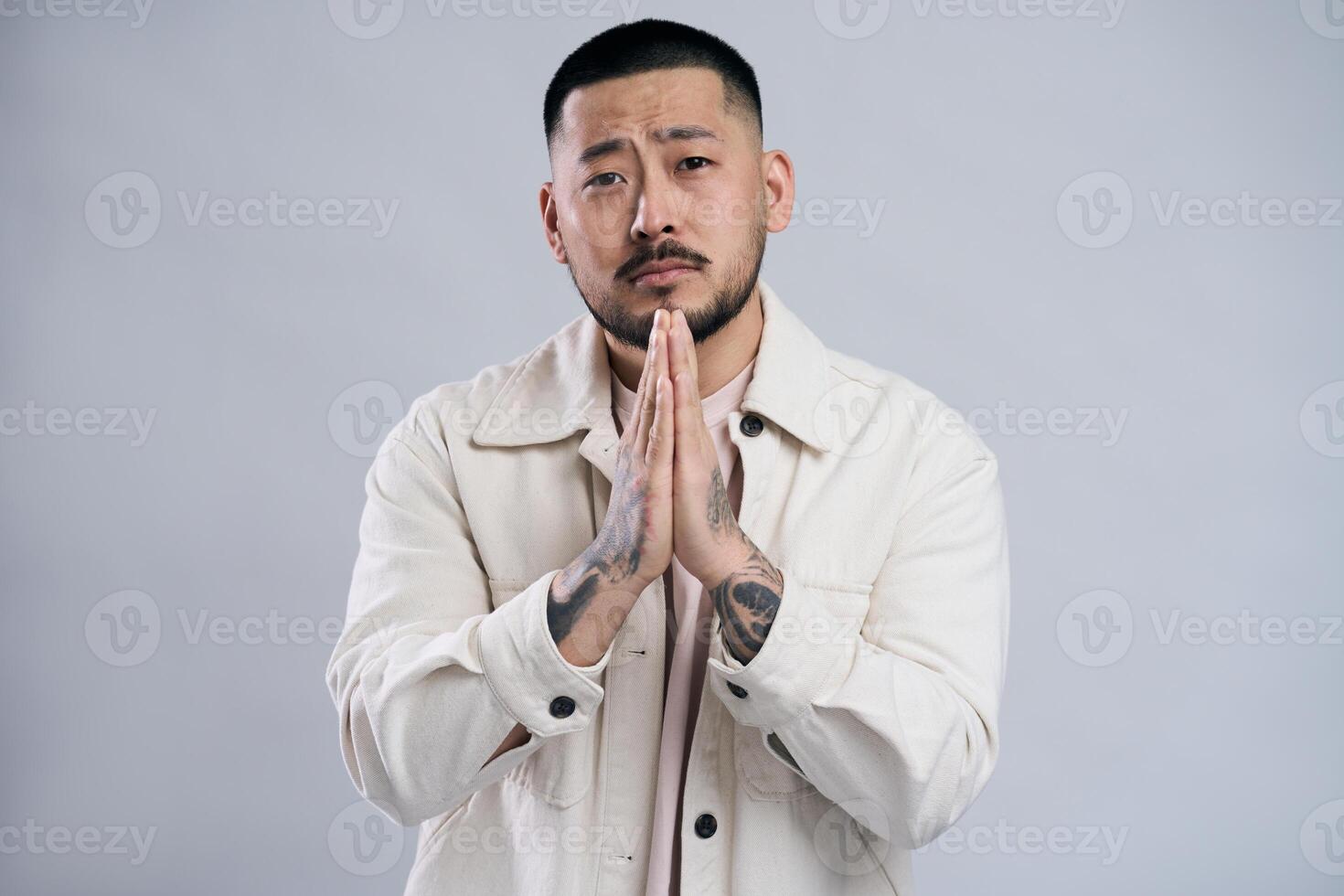 Serious young man with tattoos praying with hope photo
