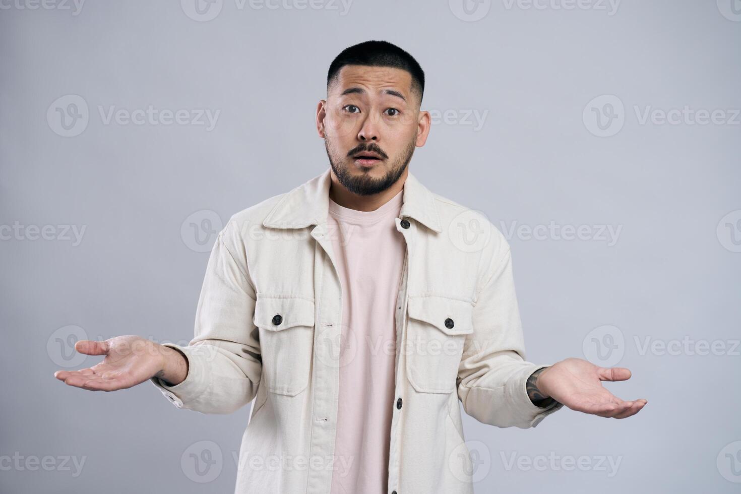Confused asian man shrugging with open palms posing in studio photo