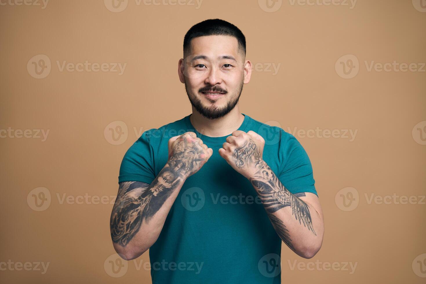 Young tattooed man showing fists on brown background photo
