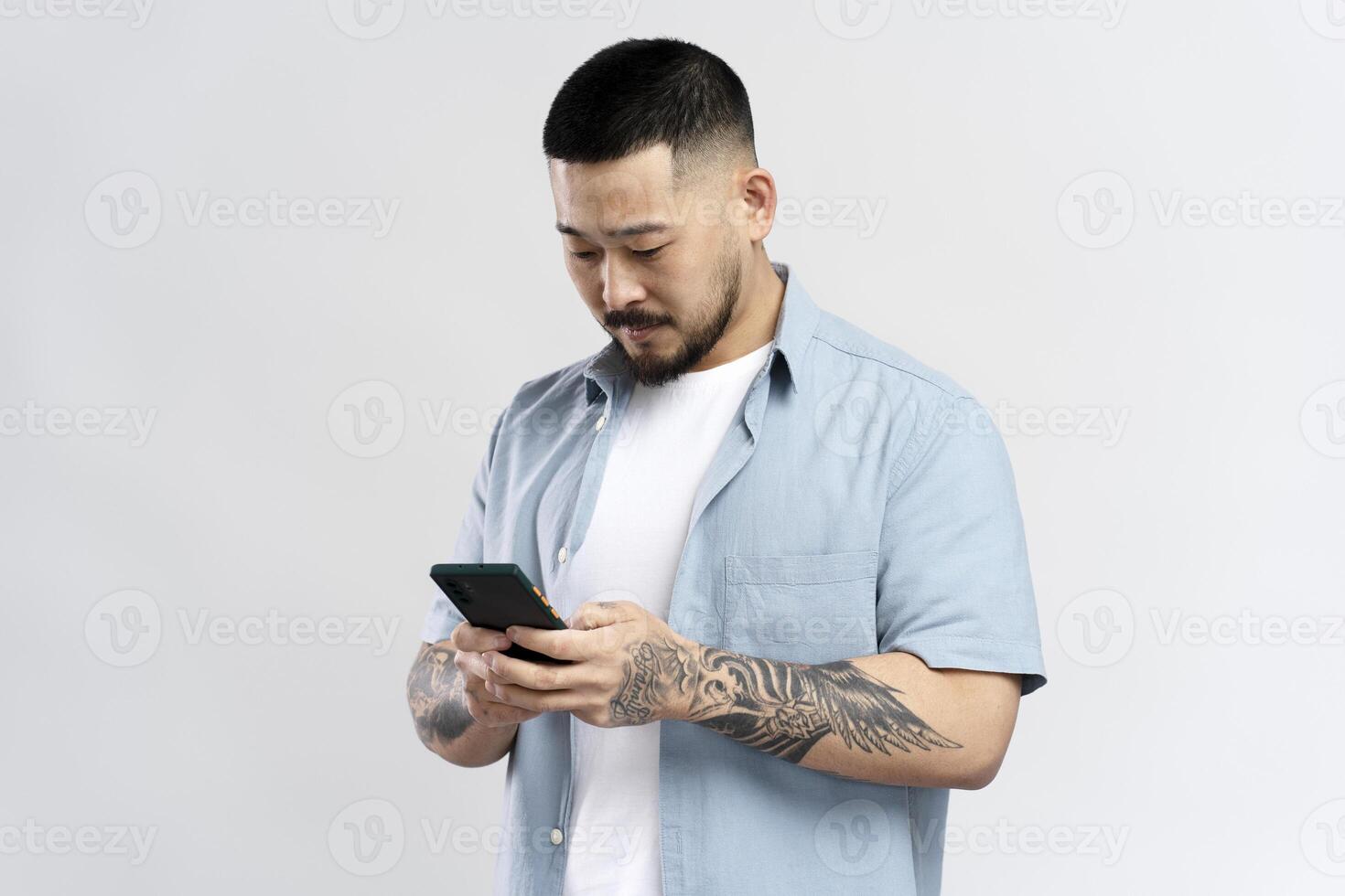 Asian man with tattoos is using smartphone on white background photo